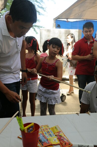 Faith Tan, 8, and her father, Maj. Roy Tan, 425th Fighter Squadron assistant director of operations, play a game called key fishing during the Singapore National Day Aug. 5 at Club Five Six. The goal was to retrieve all the keys from the edge of a table using a “fishing pole” as fast as possible. (U.S. Air Force photo by Senior Airman Tracie Forte)