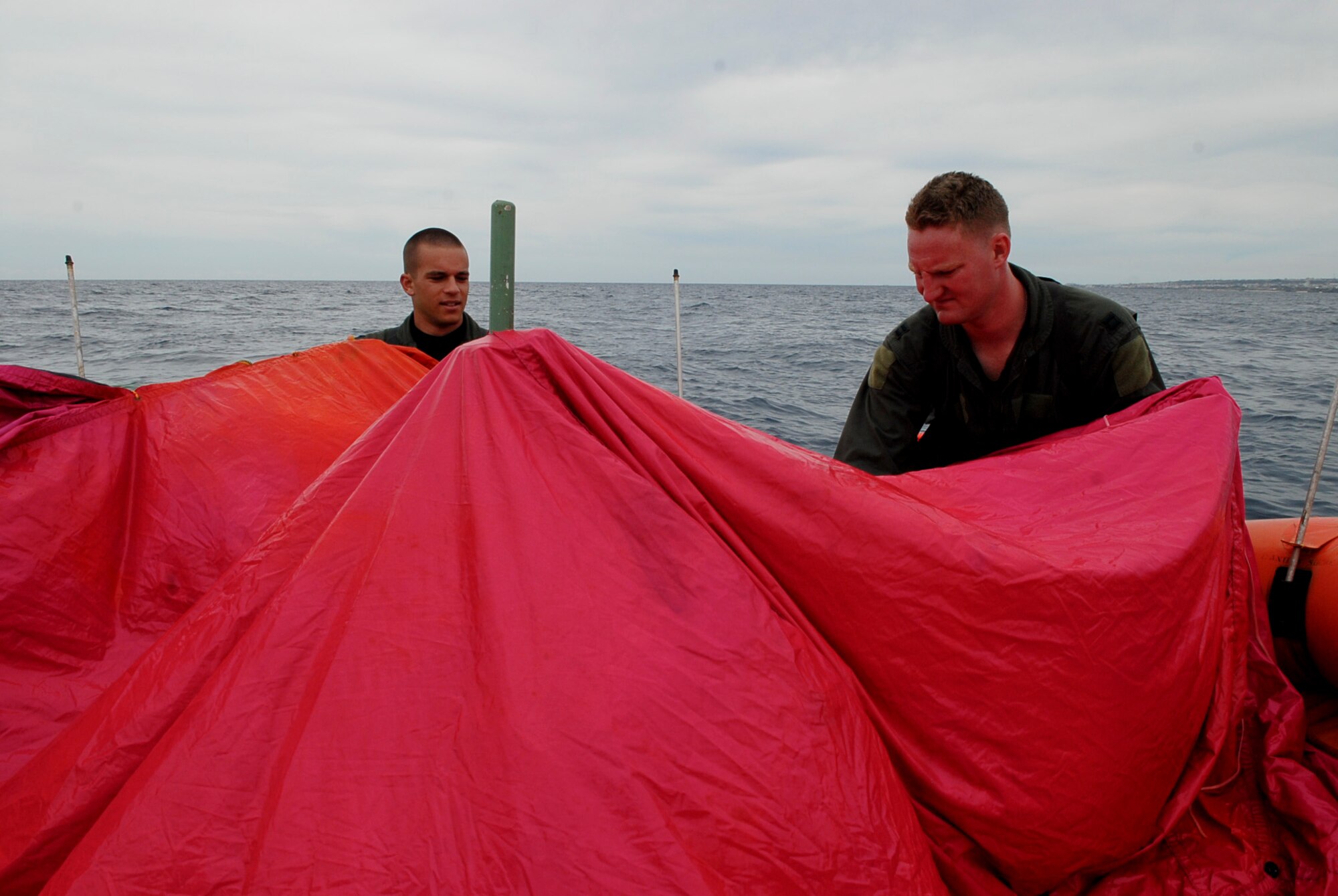 Capts. Chris Moran and Travis Epp, 909th Air Refueling Squadron KC-135 pilots, find the edges of a tarp from a survival kit to make a canopy over a life raft during a water survival refresher course Aug. 11 at the Kadena Marina in Okinawa, Japan. This survival course is required every three years for aircrew members to familiarize themselves with the equipment and skills needed if they find themselves making a water landing. (U.S. Air Force photo/ Airman 1st Class Tara A. Williamson)