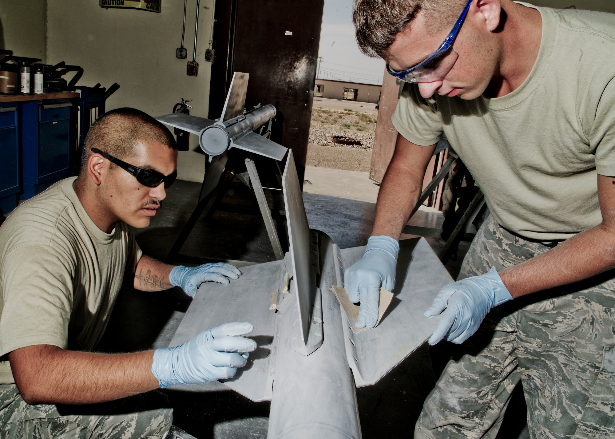 HOLLOMAN AIR FORCE BASE, N.M. -- U.S. Air Force Senior Airmen Robert Thomas and Justin Crawford, both from the 49th Maintenance Squadron’s conventional munitions flight, use sandpaper to smooth the surface of an AIM-9 missile Aug. 15, 2011. After sanding down all bare surfaces on AIM-9 missiles, they are coated with primer before being sprayed with a final coat of paint. Airmen from the conventional maintenance element prepare these missiles every six months as part of a periodic inspection to protect them from weather damage. (U.S. Air Force photo by Senior Airmen Veronica Stamps/Released)