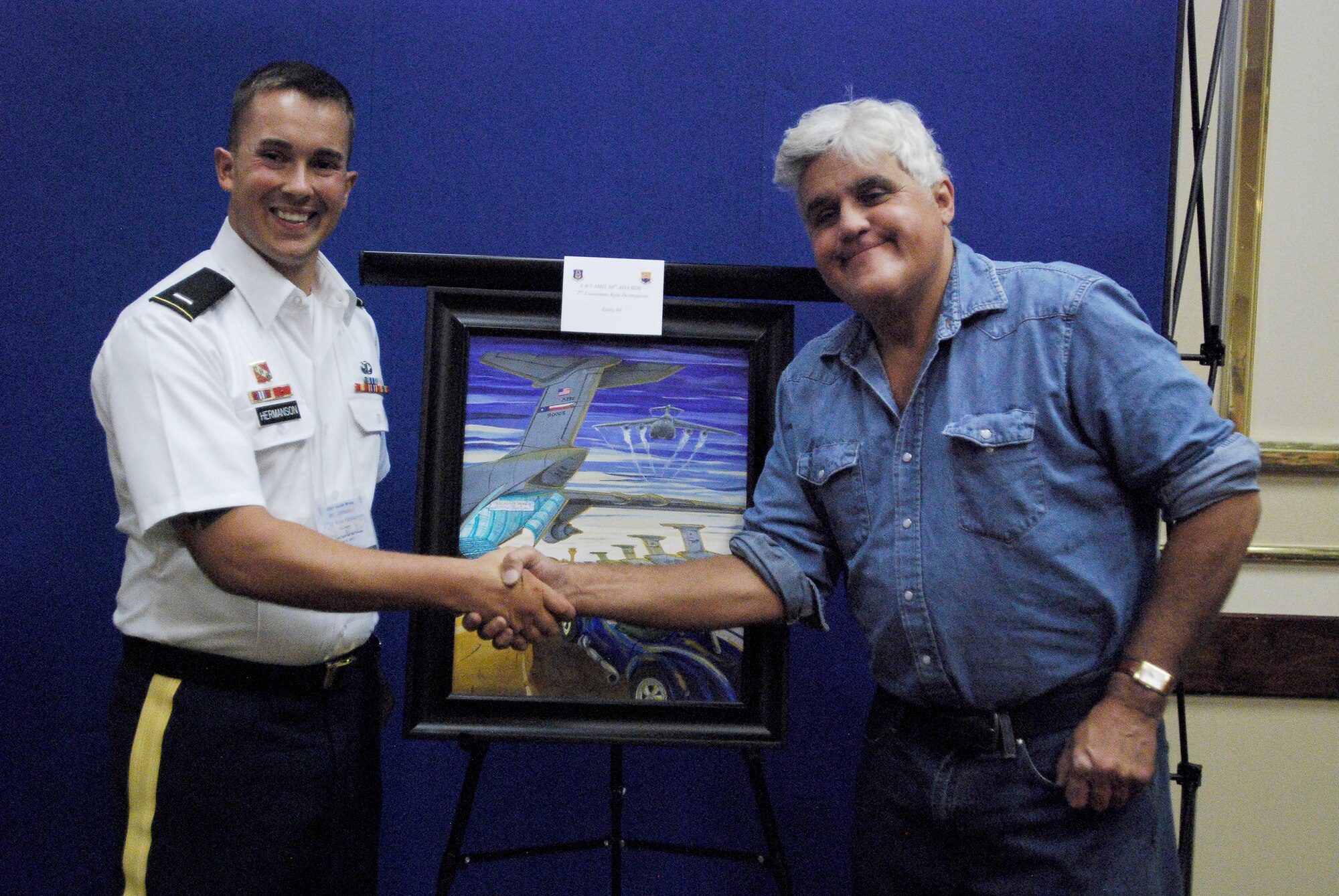 Army 1st Lt. Kyle Hermanson shakes hands with TV host and comedian, Jay Leno, while posing for a phot next to the painting entered by Lt. Hermanson for the 433rd Airlift Wing's Jay Leno Art Contest, which took place during a pre-show reception, Aug. 6, 2011, at the Kelly Field Club at Port San Antonio. The Army officer took first place in the art competition. He is currently a member of the 69th Air Defense Brigade at Ft. Hood, Texas and his wife, Allison, a staff sergeant with the 433rd Aeromedical Evacuation Squadron, an Air Force Reserve unit at Lackland Air Force Base, Texas.  (U.S. Air Force photo/Senior Airman Brian McGloin) 