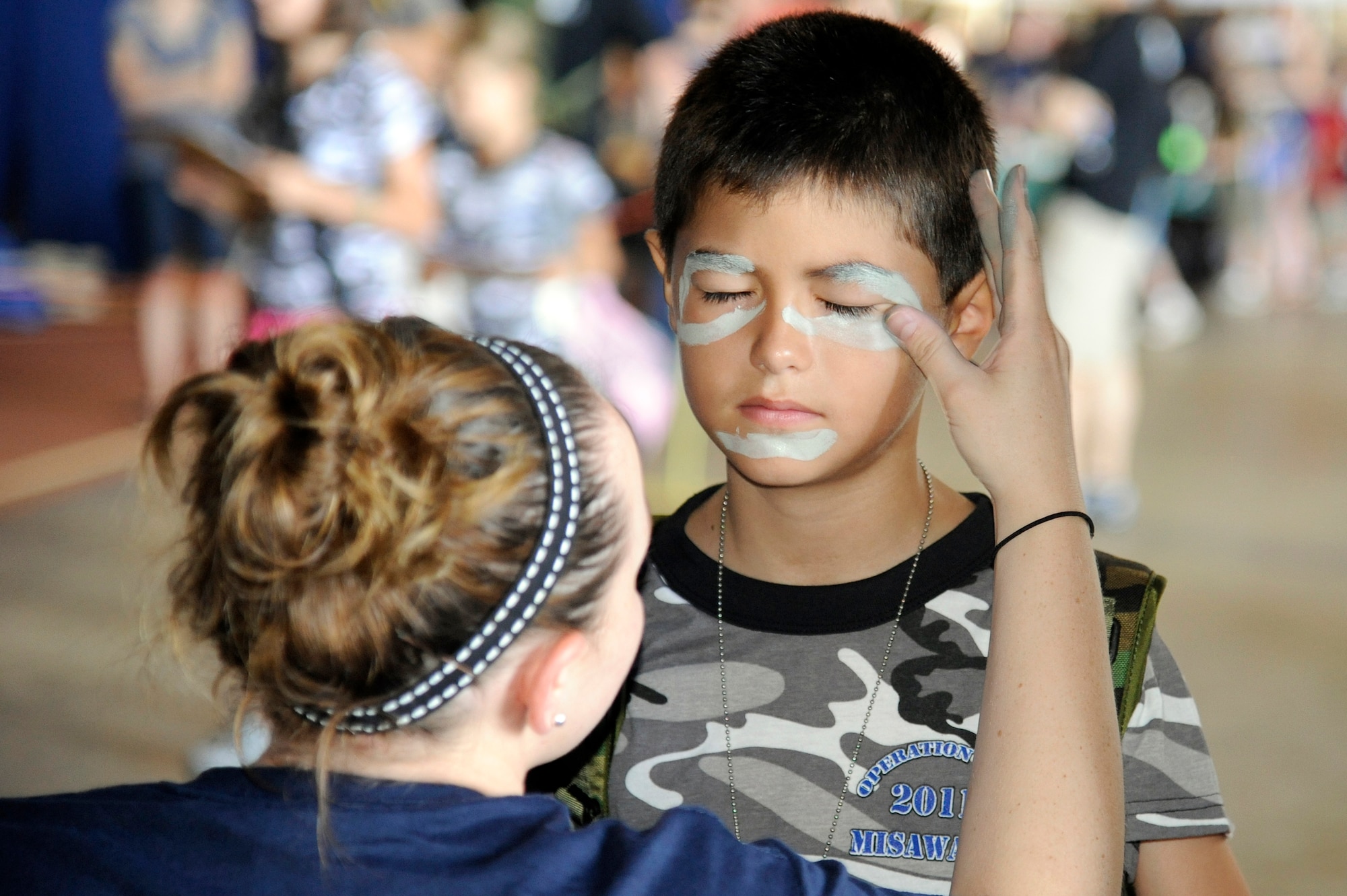 MISAWA AIR BASE, Japan -- Brittany Goldwing, left, applies face paint to Christian Colburn, son of Tech. Sgt. Shawn Colburn, 35th Maintenance Squadron, during Operation Children on Deployment Exercise Aug. 13. All children participating in the exercise were recalled at 0700 in order to process through the deployment line. (U.S. Air Force photo/Tech. Sgt. Marie Brown)