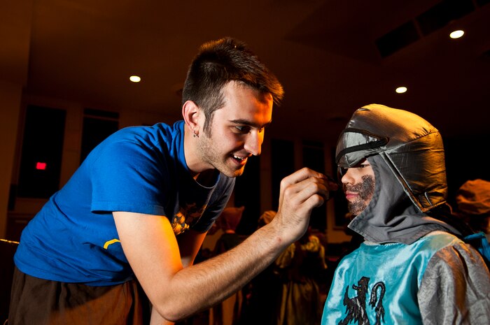 Ross Egan, Missoula Children's Theater tour actor and director, applies make-up to Mini Sir Lancelot, played by Logan Tuggle, son of Kathleen Tuggle and Tech. Sgt. Winston Tuggle, 372nd Training Squadron Detachment 13 instructor, before show time Aug. 12, 2011, in the Base Theater at Nellis Air Force Base, Nev. Logan Tuggle was one of 59 Nellis children who participated in the MCT musical "King Arthur's Quest," which tells a story of King Arthur, the Knights of the Round Table and the people of Camelot and how they deal with troubles that include being visited by the ghost of King Arthur's father, being confronted by a giant and being terrorized by a dragon. (U.S. Air Force photo by Airman 1st Class George Goslin/Released)