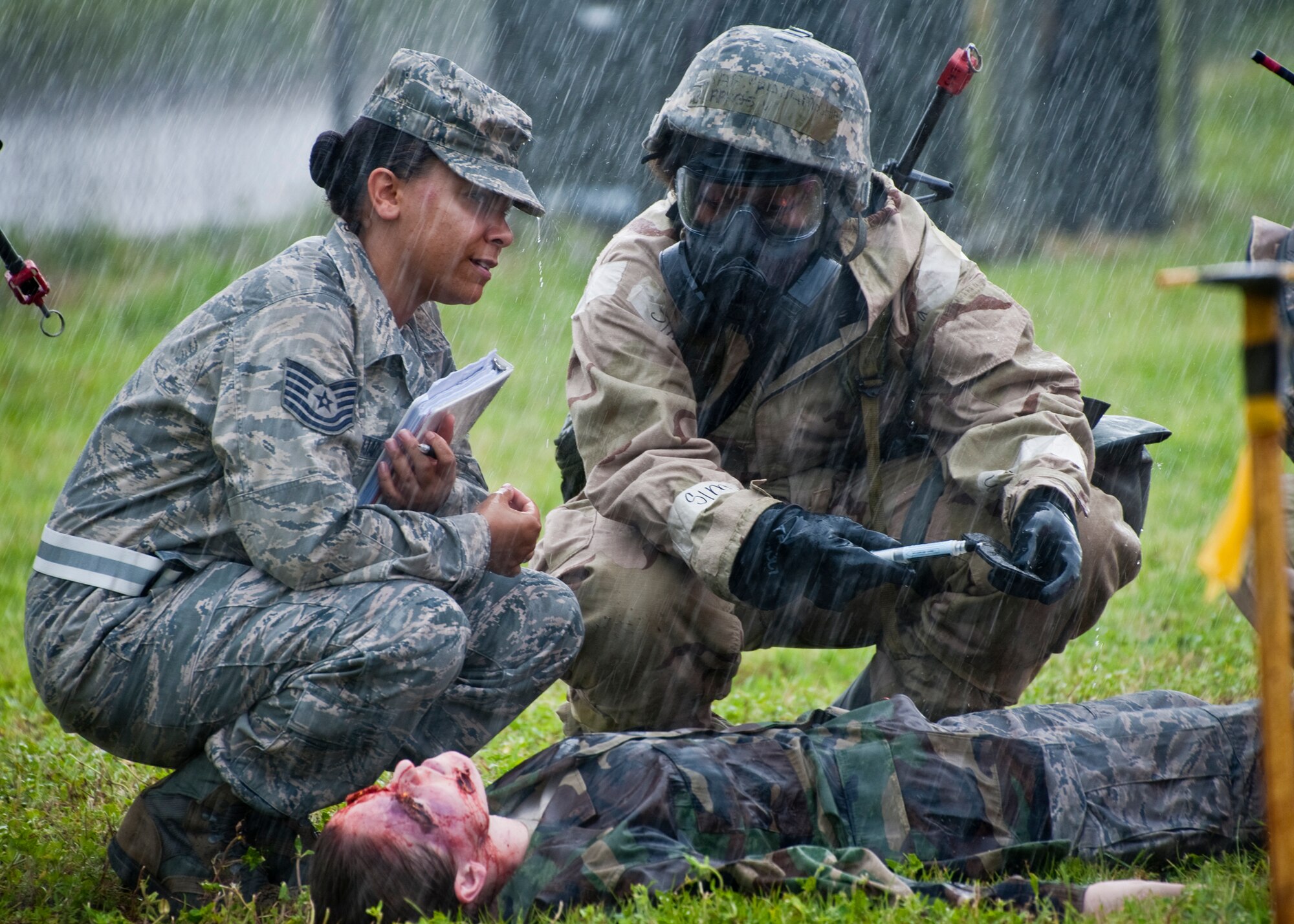 Tech. Sgt. Julia Andujar, 96th Aerospace Medicine Squadron, talks out a plan of action with an Airman through a sudden rainstorm during the Phase II exercise Aug. 10 at Eglin Air Force Base, Fla.  More than 100 Airmen braved black flag conditions (and rain) in chemical gear and gas masks to execute self-aid and buddy care, security and chemical attack avoidance missions.  The Phase II was part of a large week-long Operational Readiness Exercise on base.  (U.S. Air Force photo/Samuel King Jr.)