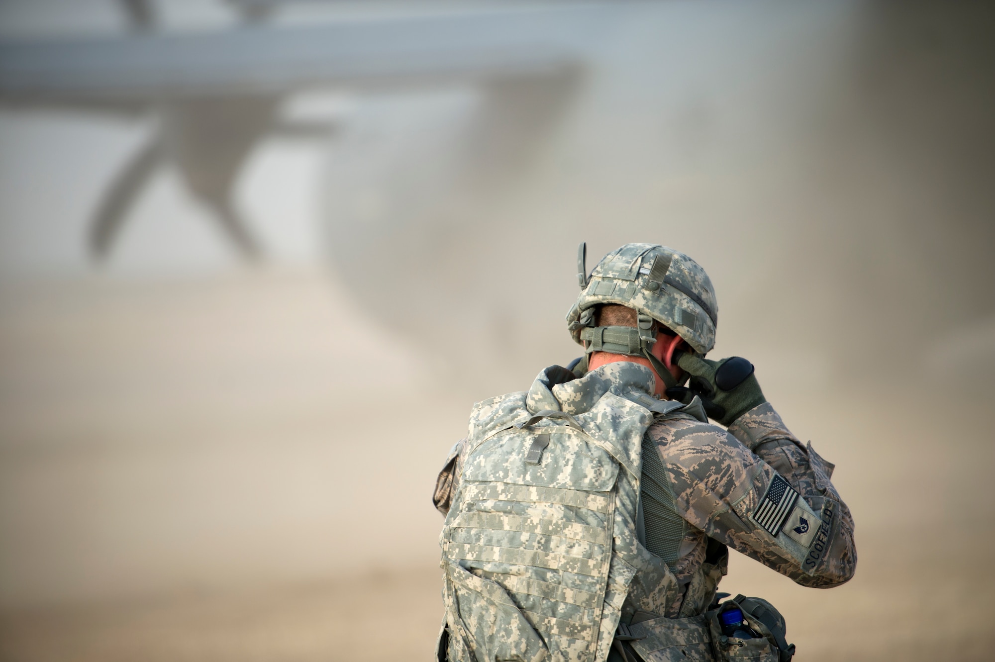 U.S. Air Force Staff Sgt. Aaron Scofield, a firefighter with the quick strike team, covers his ears as a C-130 taxis down a dirt runway near Forward Operating Base Apache, Afghanistan, Aug. 12, 2011. The C-130 delivered the last of the firefighter's P-19 fire engines. The firefighters are part of a team, deployed to set up crash, fire and rescue at a bare base. (U.S. Air Force photo by Staff Sgt. David Salanitri) 