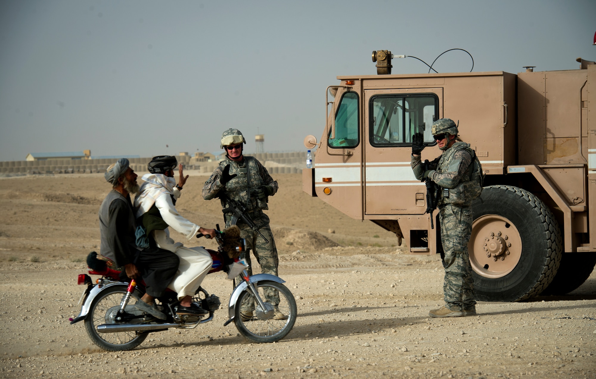 From left, U.S. Air Force Tech. Sgt. Gabriel Johnson, deputy fire chief, and Staff Sgt. Aaron Scofield, wave at two Afghan men as they ride by their truck, Aug. 12, 2011 near Forward Operating Base Apache. The firefighters were providing crash, fire and rescue support for a C-130 that was delivering the last of the firefighter's P-19 fire engines. The firefighters are part of a team, deployed to set up crass, fire and rescue at a bare base. (U.S. Air Force photo by Staff Sgt. David Salanitri)