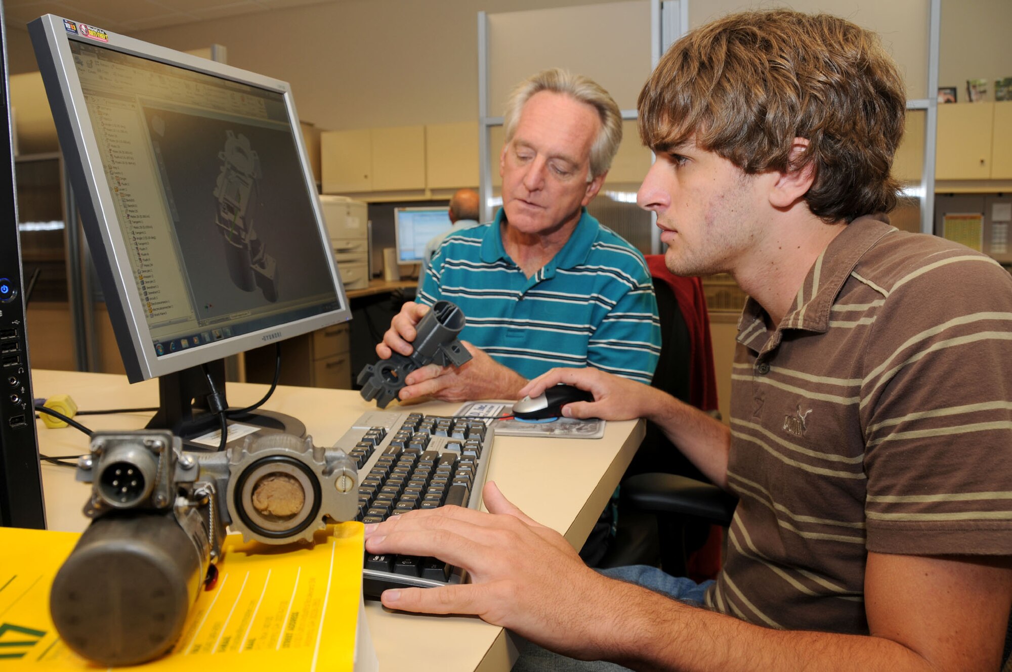 Paul Peterson, left, 81st Training Support Squadron mechanical designer, and Levi DeLuke, intern, are stepping through the process of reverse engineering the fire extinguisher valve on a C-130 August 15. DeLuke is entering measurements into 3-D modeling software which will be used to fabricate a trainer for Sheppard.  (U.S. Air Force photo by Kemberly Groue)