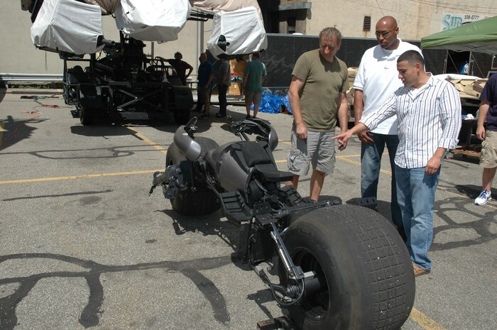 Andy Simm, a mechanic for the new Batman movie The Dark Knight Rises  explains components of Batman’s motorcycle to Army Staff Sgt. Billy Moore and Marine Sgt. Gabriel Ledesma, during a visit to the movie set in Pittsburgh, Aug. 17.