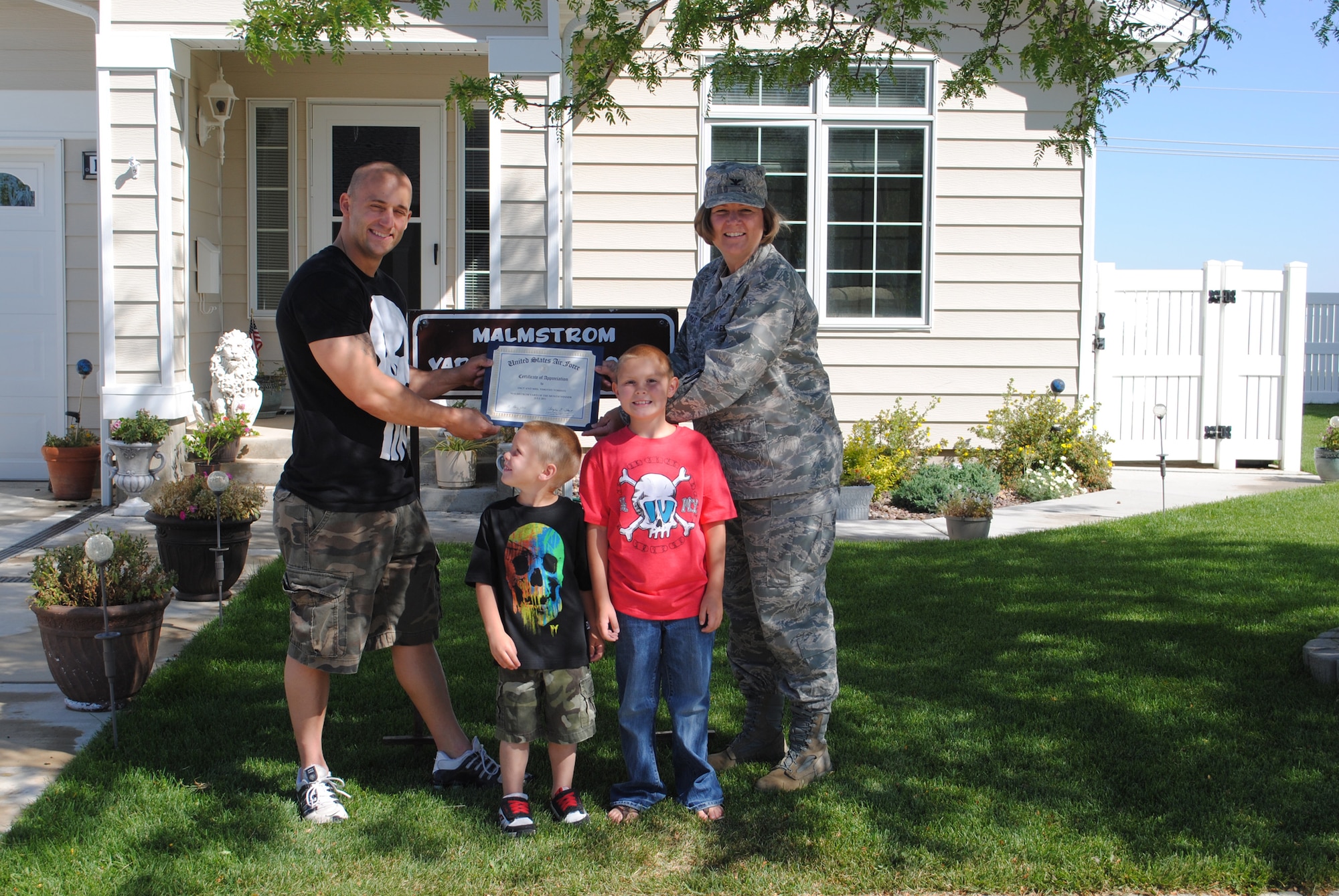 Col. Angela Stout, 341st Mission Support Group commander, presents a certificate to Staff Sgt. Tim Vorhies, 341st Security Forces Group supply custodian/facility manager, his two boys Logan; 4, and Bryan; 7, and his wife, Laura (not present), at their residence of 1218 Walnut for the Yard of the Month for July.  Along with the certificate from the commander, the family also recieved a gift certificate to AAFES and are eligable to compete in the Yard of the Year competition in September.  (U.S. Air Force photo/Airman Cortney Paxton)