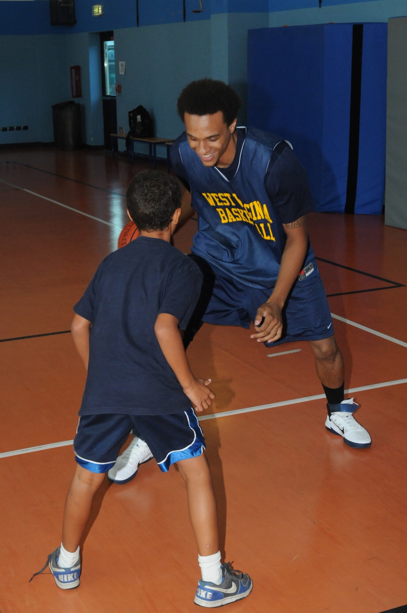 West Virginia University forward Tommie McCune plays one-on-one with an Aviano Youth Center member Aug. 17 during a basketball clinic at the center gymnasium. Players of West Virginia University Mountaineers and the Illinois Univerisity Fighting Illini taught basketball techniques to more than 40 children. (U.S. Air Force photo/Airman LaVel Sterling)