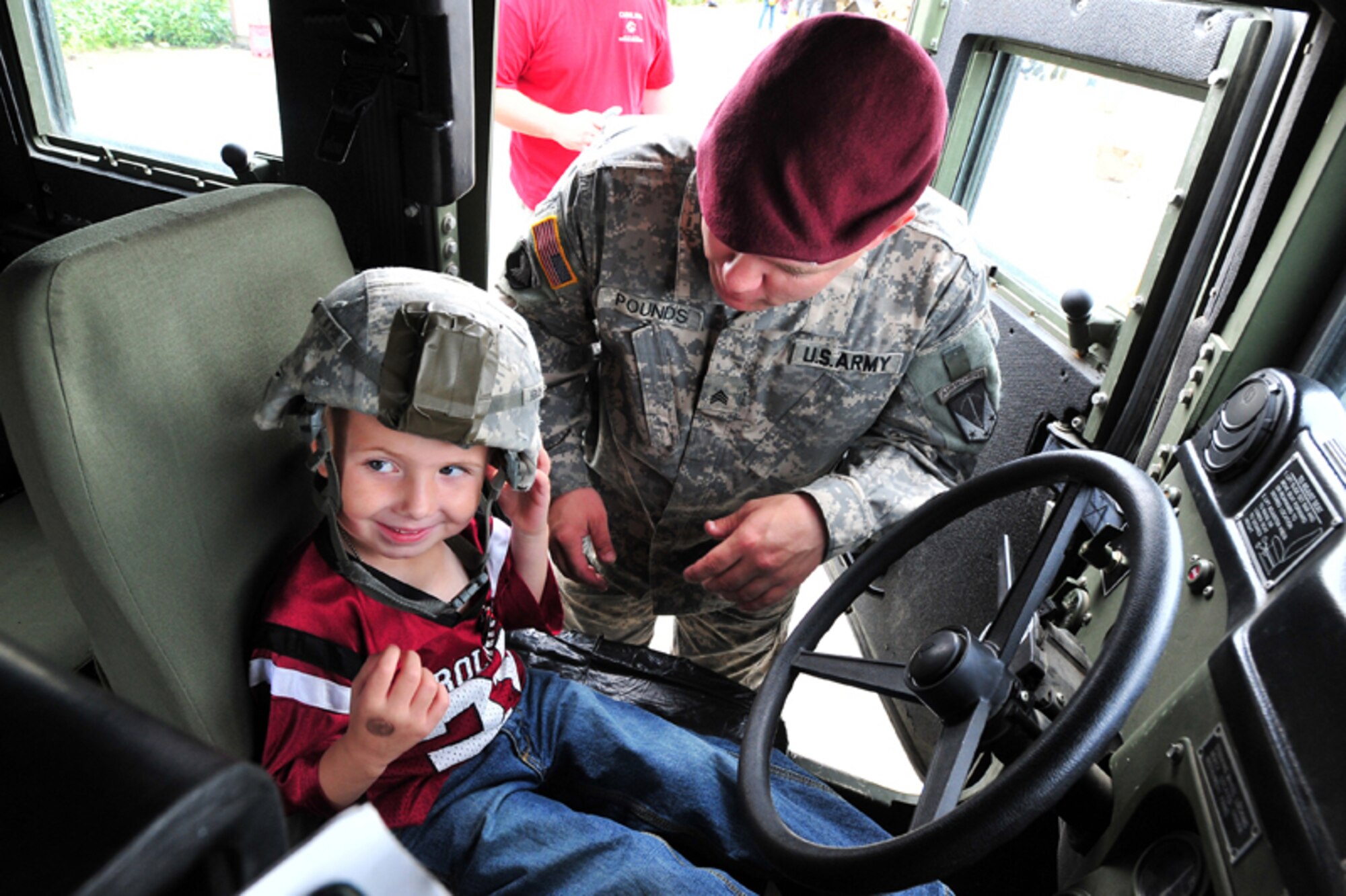 Sgt. James Pounds, 84th Engineer Support Company, of Camden, N.Y., puts a helmet on Trey Richardson, 4, inside a Humvee during the Operation: Arctic Warrior event for children and families at the Joint Mobility Complex Saturday. Children experienced a mock deployment, displays and enjoyed lunch during the event.  (U.S. Air Force photo/Justin Connaher)