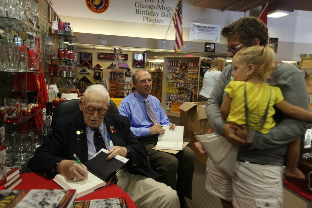 Retired Maj. Norman Hatch, signs a book for a former combat cameraman during A book signing event at the Marine Corps Association Bookstore aboard Marine Corps Base Camp Lejeune, Aug. 18. Hatch was a combat cameraman who served in World War II. His video and photographs played a crucial role in keeping the Marine Corps from being disbanded after WWII.