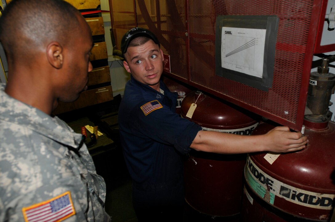 Pvt. Garth Longmore (left) receives instruction from Sgt. David Compton, Army watercraft engineer assigned to the 335th Transportation Detachment, 24th Transportation Battalion, on how to take a reading of the FM-200 Fire Suppression system on board the U.S. Army Logistic Support Vessel-1, the Gen. Frank S. Besson Jr., Aug. 11. (US Army photo by Sgt. 1st Class Kelly Jo Bridgwater)