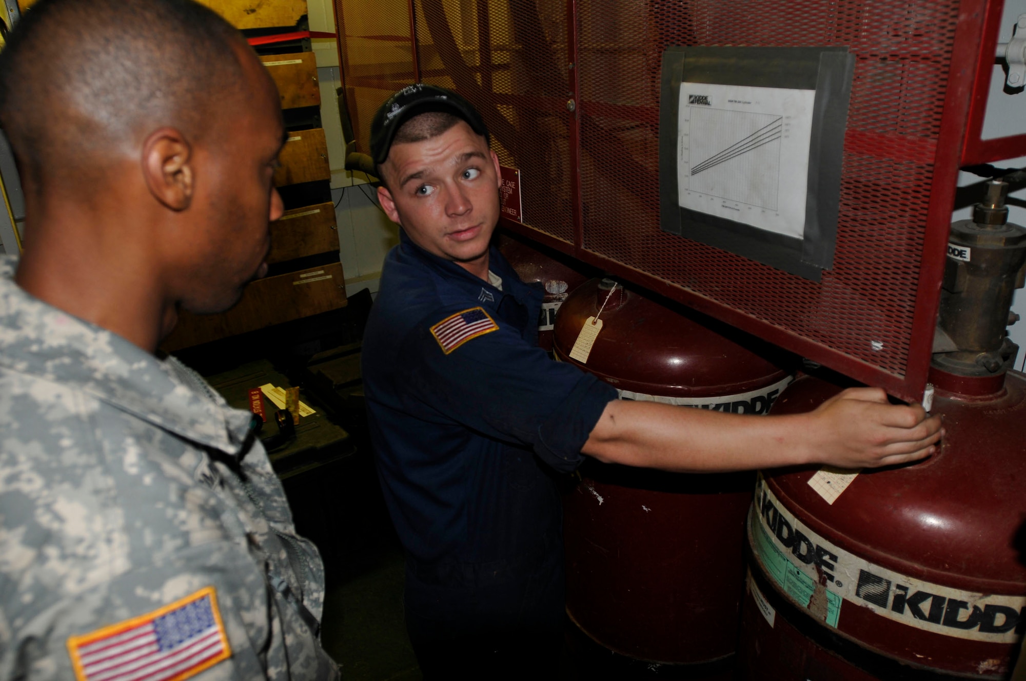 Pvt. Garth Longmore (left) receives instruction from Sgt. David Compton, Army watercraft engineer assigned to the 335th Transportation Detachment, 24th Transportation Battalion, on how to take a reading of the FM-200 Fire Suppression system on board the U.S. Army Logistic Support Vessel-1, the Gen. Frank S. Besson Jr., Aug. 11. (US Army photo by Sgt. 1st Class Kelly Jo Bridgwater)