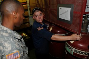 Pvt. Garth Longmore (left) receives instruction from Sgt. David Compton, Army watercraft engineer assigned to the 335th Transportation Detachment, 24th Transportation Battalion, on how to take a reading of the FM-200 Fire Suppression system on board the U.S. Army Logistic Support Vessel-1, the Gen. Frank S. Besson Jr., Aug. 11. (US Army photo by Sgt. 1st Class Kelly Jo Bridgwater)