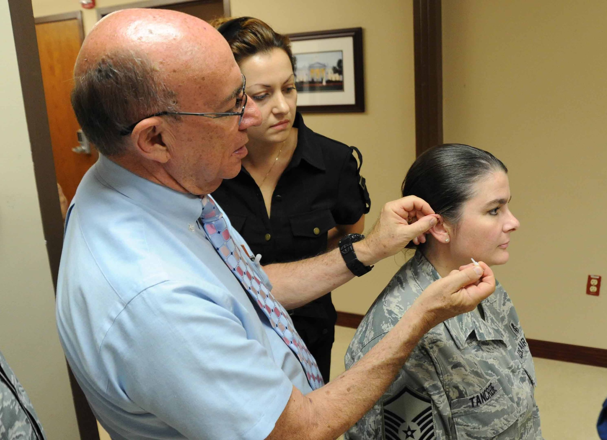 Retired Col. Richard Niemtzow, Air Force Acupuncture Clinic director, shows observing healthcare professionals how to properly apply the acupunture needle into Master Sgt. Michelle Tancrede’s, 779th Aerospace Medical Squadron mission operations NCO in charge, ear during the battlefield acupuncture course here Aug. 12. Battlefiled acupuncture is a simple easy to use technique that offers fast and effective pain relief. (U.S Air Force photo/ Bahja J. Jones) 