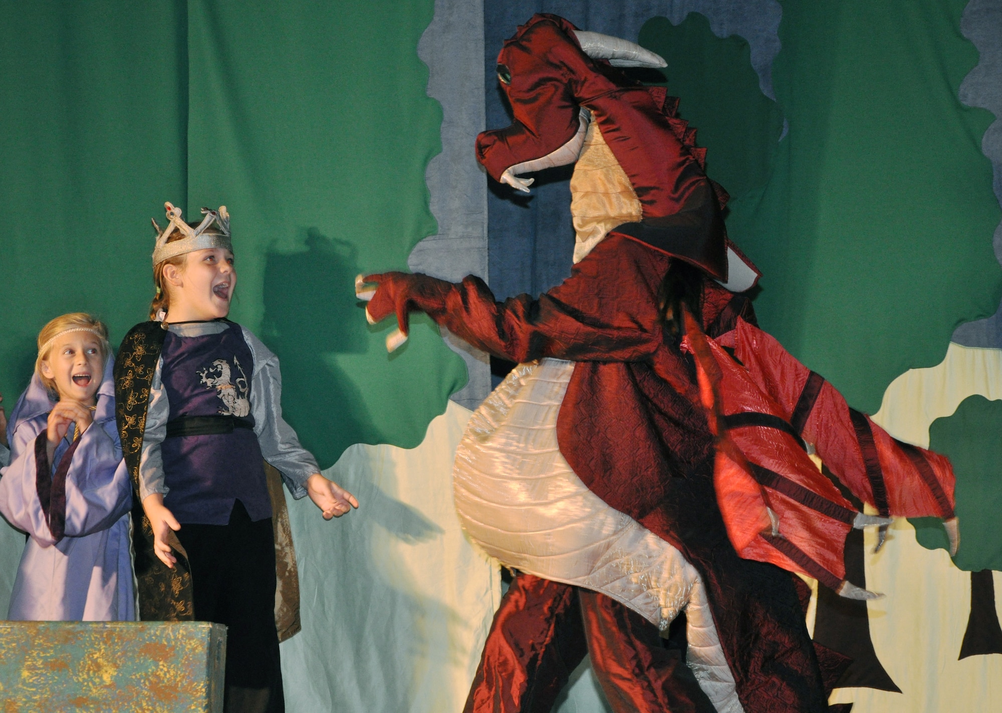 GOODFELLOW AIR FORCE BASE, Texas -- (From left:) Molly Willis, mini Guinevere, and Elise Hunnemeyer, mini King Arthur, are frightened by a dragon they encounter while walking through the woods during the Missoula Children's Theatre's production of King Arthur's Quest Aug. 19 at the base theater.  More than 50 base youths participated in this year's play, which was cast and produced in five days. (U.S. Air Force photo/Connie Hempel)