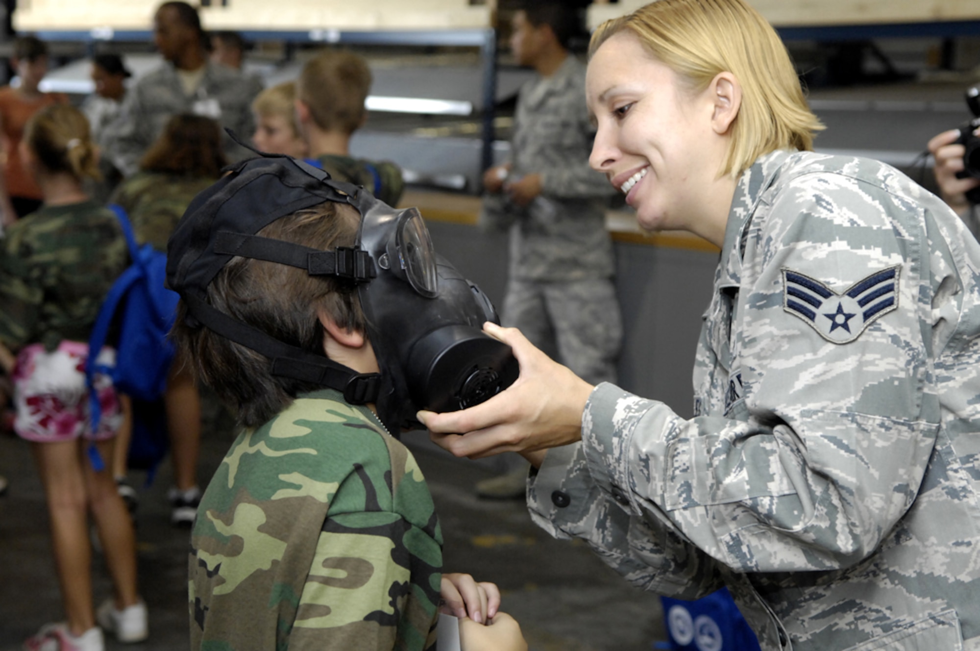 Senior Airman Sally Morales, 647th Civil Engineer Squadron Emergency 
Management specialist, assists Donovan Castillo with his gas mask in the mobility 
processing line during Operation Hele-On, a mock deployment for military families at Joint Base Pearl Harbor-Hickam, Hawaii, Aug 19. 155 children participated in the annual event, which included getting mobility bags and "gear" issued, getting bussed to the flight line, and a tour of the KC-135. This experience was geared to help children understand what their parents go through during a real military deployment. (U.S. Air Force photo/David D. Underwood, Jr.)
