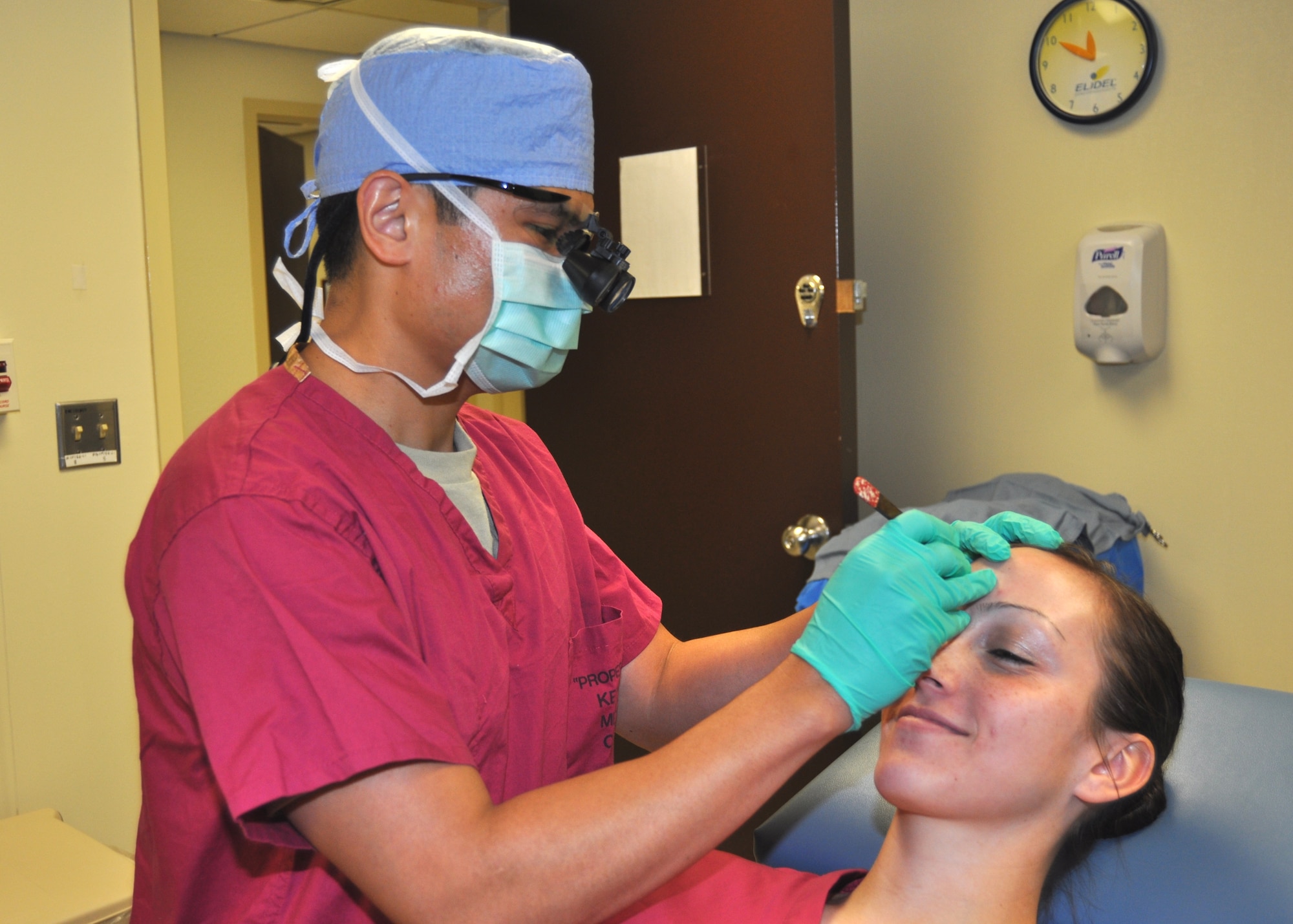 Dr. Wisco simulates removing skin cancer from “patient” Senior Airman Kayla Spiel, a dermatology clinic medical technician. In an actual procedure, the tissue would be frozen, placed on a slide and reviewed. If Wisco finds there’s still cancer at the site, he would remove it as well.  (U.S. Air Force photo by Steve Pivnick)
