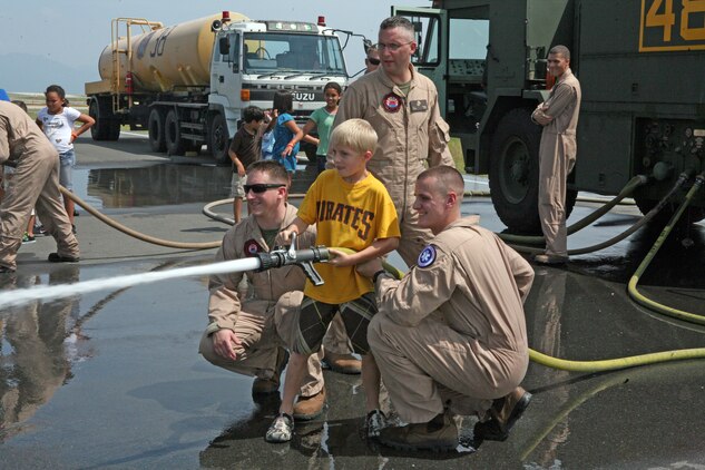 Gunnery Sgt. Shane S. Smoger, Aircraft Rescue and Firefighting section leader and event coordinator, watches as Sgt. Matthew L. Tinsley and Lance Cpl. Andrew R. Pepe, ARFF specialists, assist Paden White, 8-year-old with the Camp Adventure program at School Age Care, to control the fire hose during the second annual station airfield operations facilities tour here Aug. 25. The children were part of the Camp Adventure a SAC summer school program , which provides recreational activities, sports camps, field trips and educational programs.