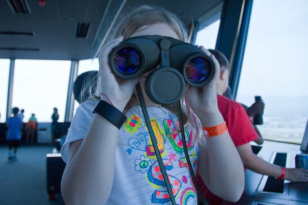 Julia Good, 8-year-old with the Camp Adventure program at School Age Care, uses binoculars to look at the view from the air traffic control tower during the 2nd annual tour of the station airfield operations facilities here Aug. 25. Children also toured Aircraft Rescue and Firefighting facilities, the weather and flight clearance room, the terminal radar  approach control room and the air traffic control tower.