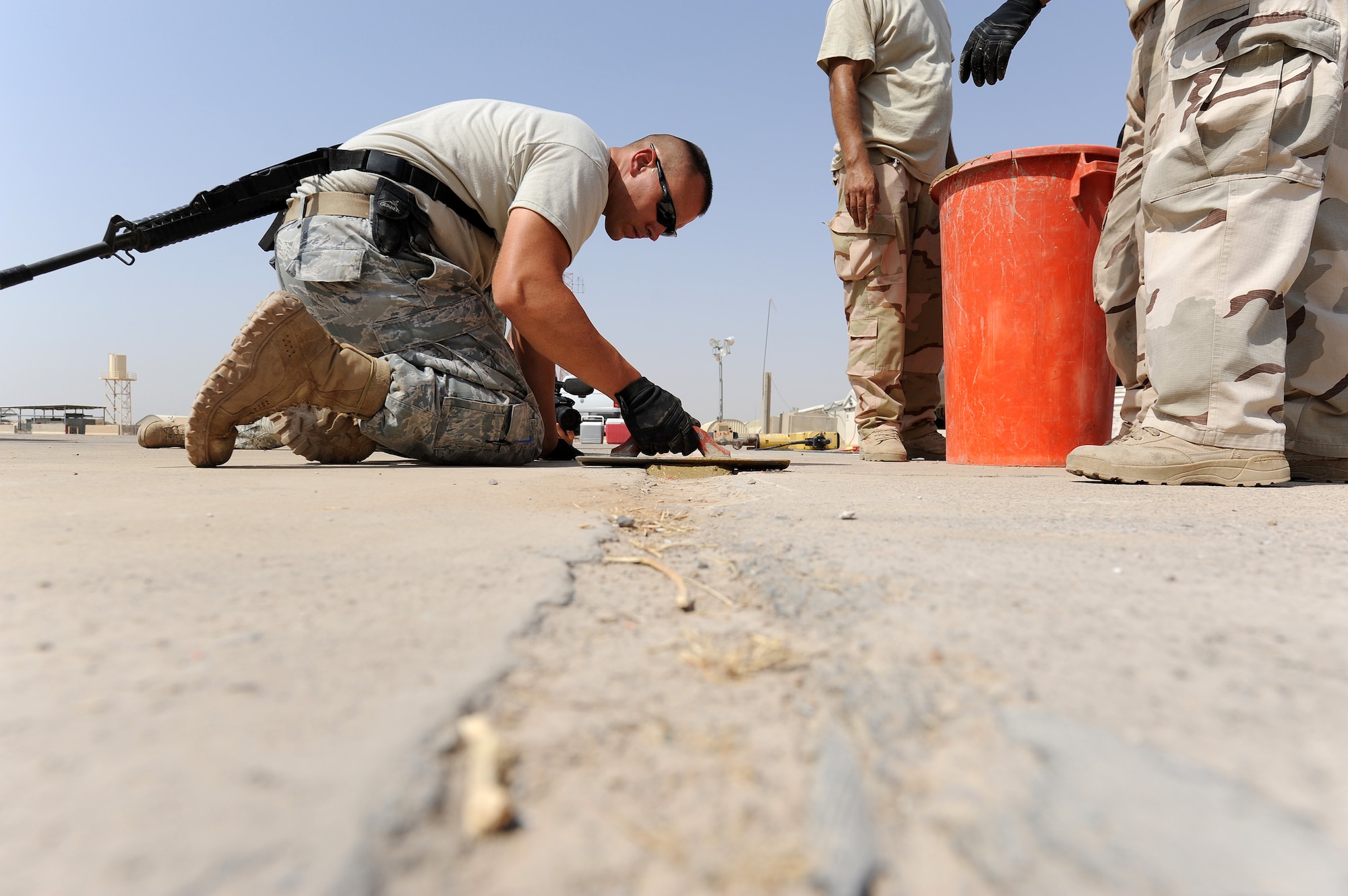 Staff Sgt. Kenneth Collins, 321st Expeditionary Operations Support Squadron, uses a trowel to help smooth out the surface of a cement mixture that was put into a hole at Kirkuk Air Base.  EOSS responds with the Iraqis, teaching them how to fix defective parts of the flight line. Without a smooth surface the aircraft will not be able to taxi the runway. (U.S. Air Force photo by Senior Airman Tristin English)