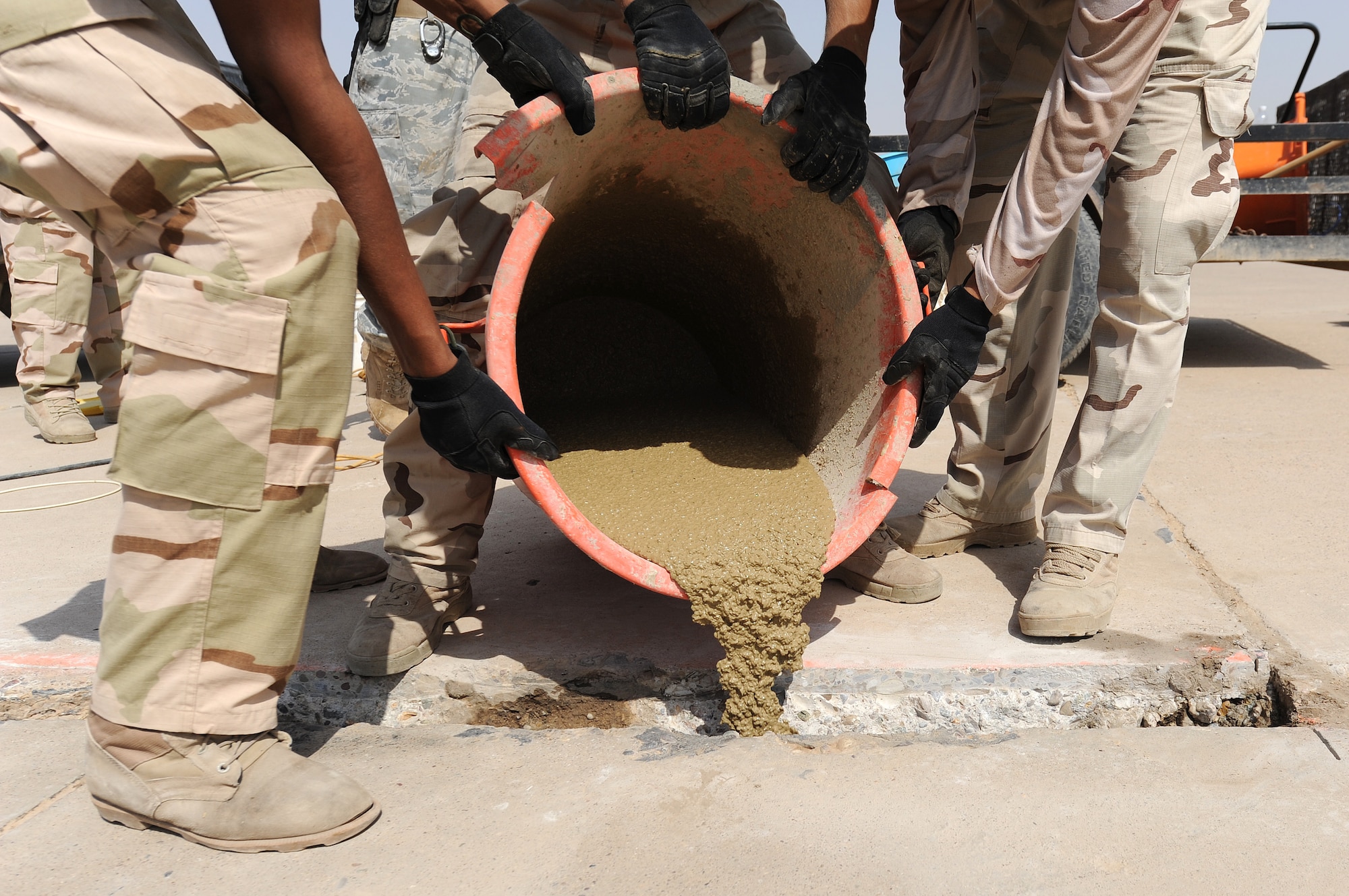 Members of the Iraqi Air Force help pour a cement mixture into a newly made hole on the flightline at Kirkuk Air Base. Over the past six months Expeditionary Operations Support Squadron has been going out on the flightline with the Iraqis teaching them how to take care of their runway.  (U.S. Air Force photo by Senior Airman Tristin English)