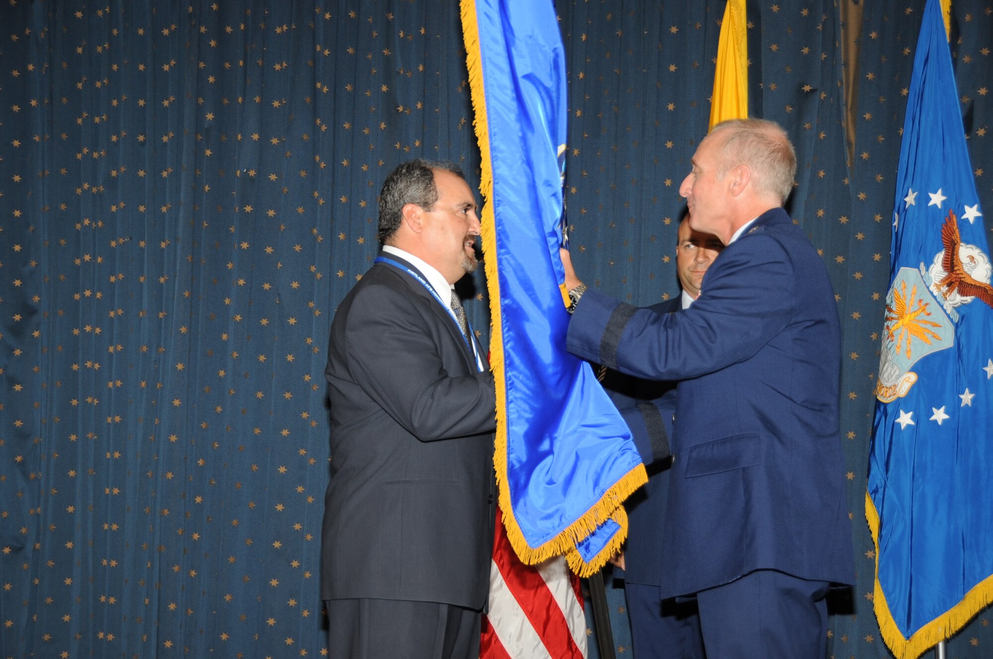 KIRTLAND AFB, N.M. -- Brig. Gen. Garrett Harencak, Air Force Nuclear Weapons Center commander, presents the guidon to his new honorary commander Carlo Lucero, Sparkle Maintenance president, during the Honorary Commanders Assumption of Command Ceremony Aug. 19 at the Mountain View Club. (photo by Dennis Carlson)