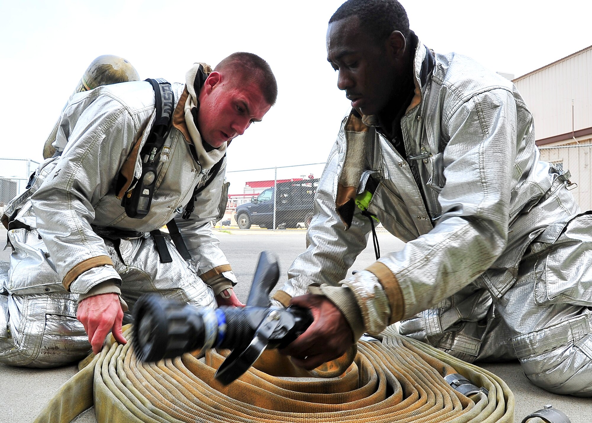(Left) Senior Airman David Brady, 51st Civil Engineer Squadron fire fighter vehicle operator and Senior Airman Jeremy Blanding, 51st Civil Engineer Squadron fire fighter, wrap a fire hose after effectively responding to a fire in building 600 Aug. 29, 2011 during exercise Beverly-Midnight. Find the fire, fight the fire and perform primary searches for victims are a few of the National Fire Protection standards the Airmen were evaluated on during the exercise. (U.S. Air Force photo/Senior Airman Adam Grant)