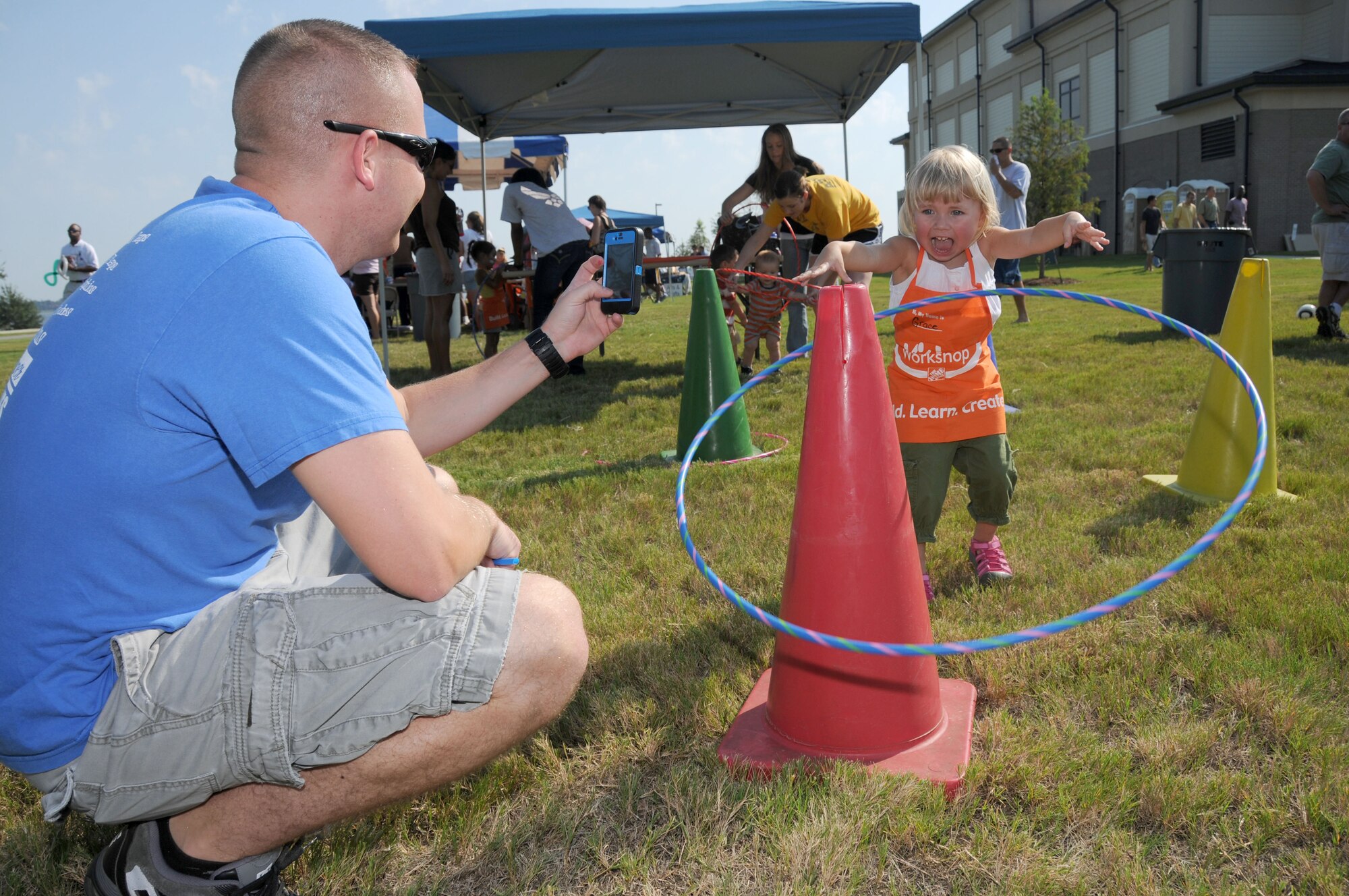 Tech. Sgt. Dan Blankenship, a Keesler firefighter, videotapes his 2 1/2 year-old-daughter, Grace, as she tosses a hula hoop around a cone at the Keesler 70th Birthday Celebration at Bay Breeze Event Center Aug. 27.  (U.S. Air Force photo by Kemberly Groue)