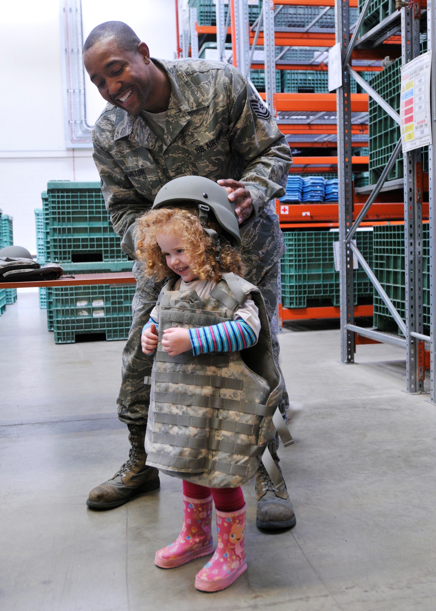 ROYAL AIR FORCE LAKENHEATH, England - Tech. Sgt. Phillip Hamilton, 48th Logistics Readiness Squadron NCO in charge of mobility, places a helmet on 3-year-old Jessica Lin Merrick at the Installation Deployment Readiness Center for a simulated deployment line, Aug. 25, 2011. The mock deployment line is designed to provide children with a better understanding of what their parents experience as they prepare for deployment. (U.S. Air Force photo/Senior Airman Tiffany M. Deuel)