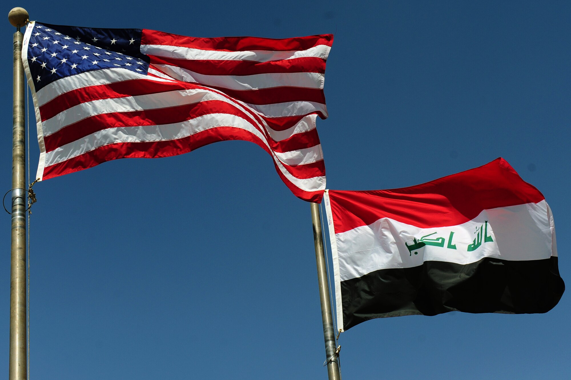 The U.S. and Iraqi flags fly in 110-degree temperatures during the official ribbon cutting ceremony of a renovated k-span serving as the new 321st Air Expeditionary Wing and Iraqi Training and Advisroy Mission-Air headquarters Aug. 28. To meet the U.S. military end of year drawdown requirement in Iraq, the former 321st AEW headquarters was turned over to the Government of Iraq in August. (U.S. Air Force photo/Staff Sgt. Mike Meares)