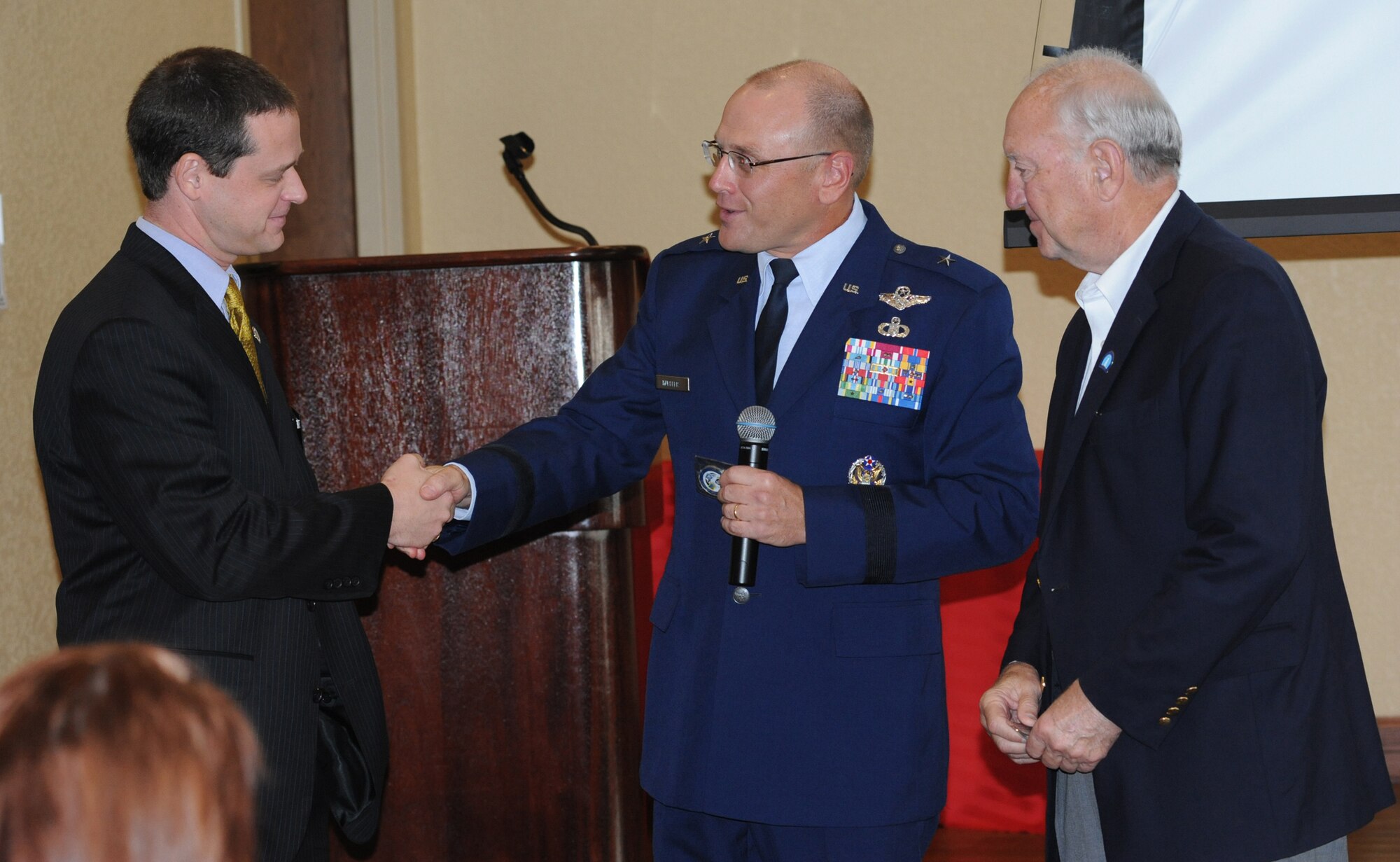 Brig. Gen. Andrew Mueller, center, 81st Training Wing commander, presents wing
coins to Bruce Marie, left, Biloxi Chamber of Commerce president, and Biloxi Mayor
A.J. Holloway. As part of its 70th birthday celebration, Keesler hosted the chamber’s
morning call at the Bay Breeze Event Center, Aug. 25.  (U.S. Air Force photo by Kemberly Groue)