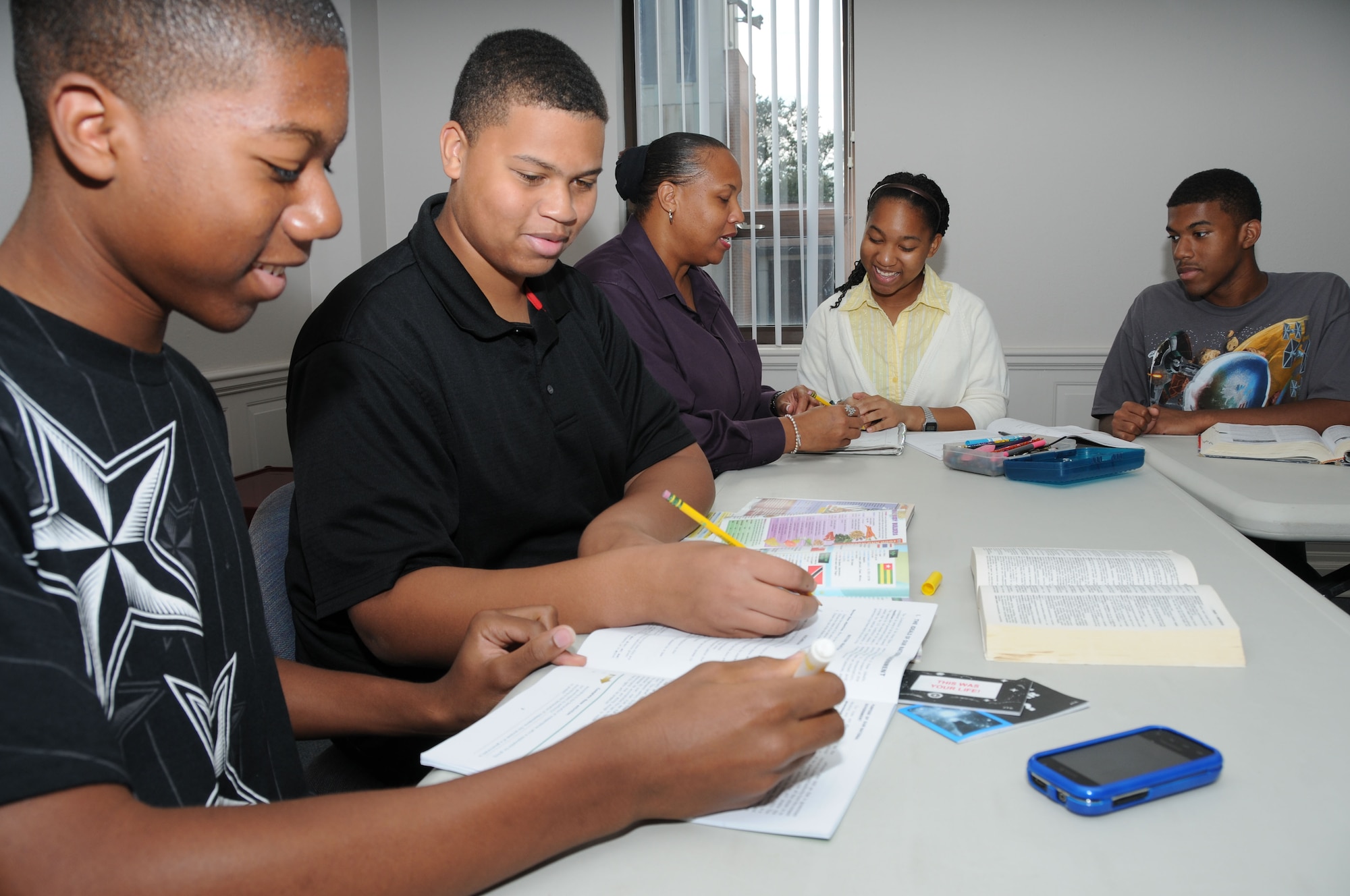 The Elliotts, from left, are William, 15; Chris, 16; Mrs. Cherie Elliott; Sydney, 13; and Ralph, 17. With mom’s help, William, Chris and Sydney review lessons prior to the start of the new school year while Ralph does some leisure reading. This home schooling session was held at the Triangle Annex because Mrs. Elliott had a gospel service leaders meeting there.  Cherie Elliott is married to Chaplain (Capt.) Ralph Elliott, who’s currently deployed.  (U.S. Air Force photo by Kemberly Groue)