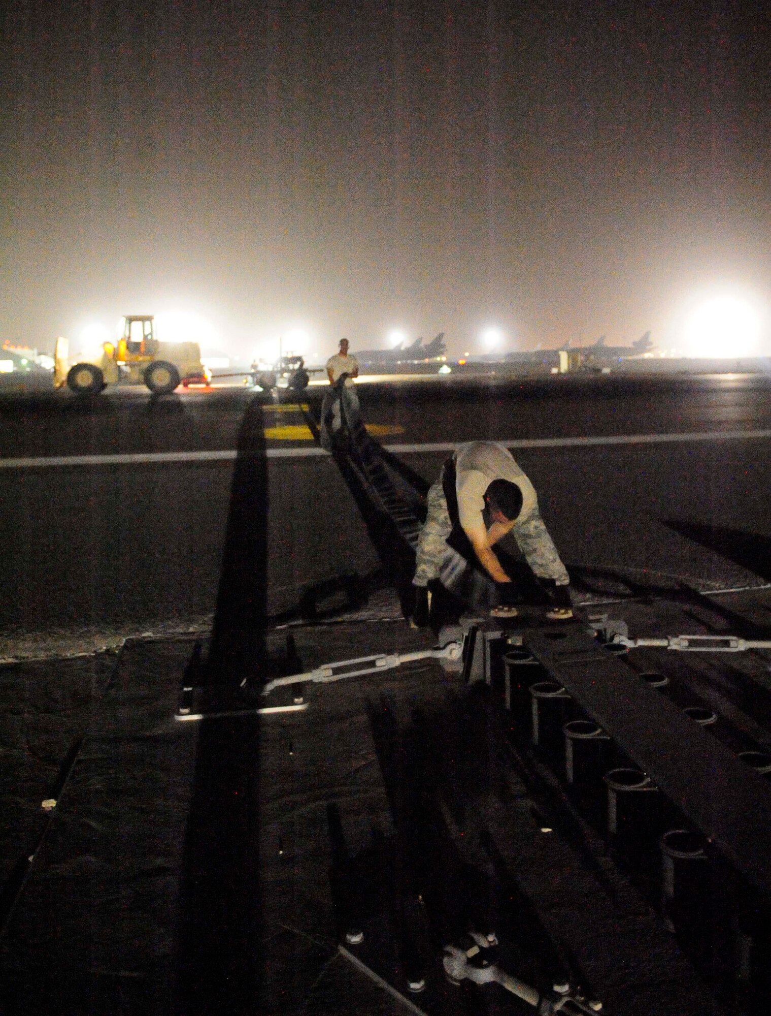 Two members from the 380th Expeditionary Civil Engineer Squadron, stretch mobile aircraft arresting system purchase tape across the flightline, Aug. 27, 2011, during a two-week maintenance overhaul of the system at an air base in Southwest Asia. This maintenance is due every 10 years. The MAAS is an emergency braking system for tail-hook-equipped aircraft. It is used in emergency situations where a fighter aircraft needs assistance with coming to a stop after flight. This occasionally occurs due to mechanical failures beyond the pilot's abilities to correct prior to landing.  (U.S. Air Force photo/Tech. Sgt. Patrick Mitchell)