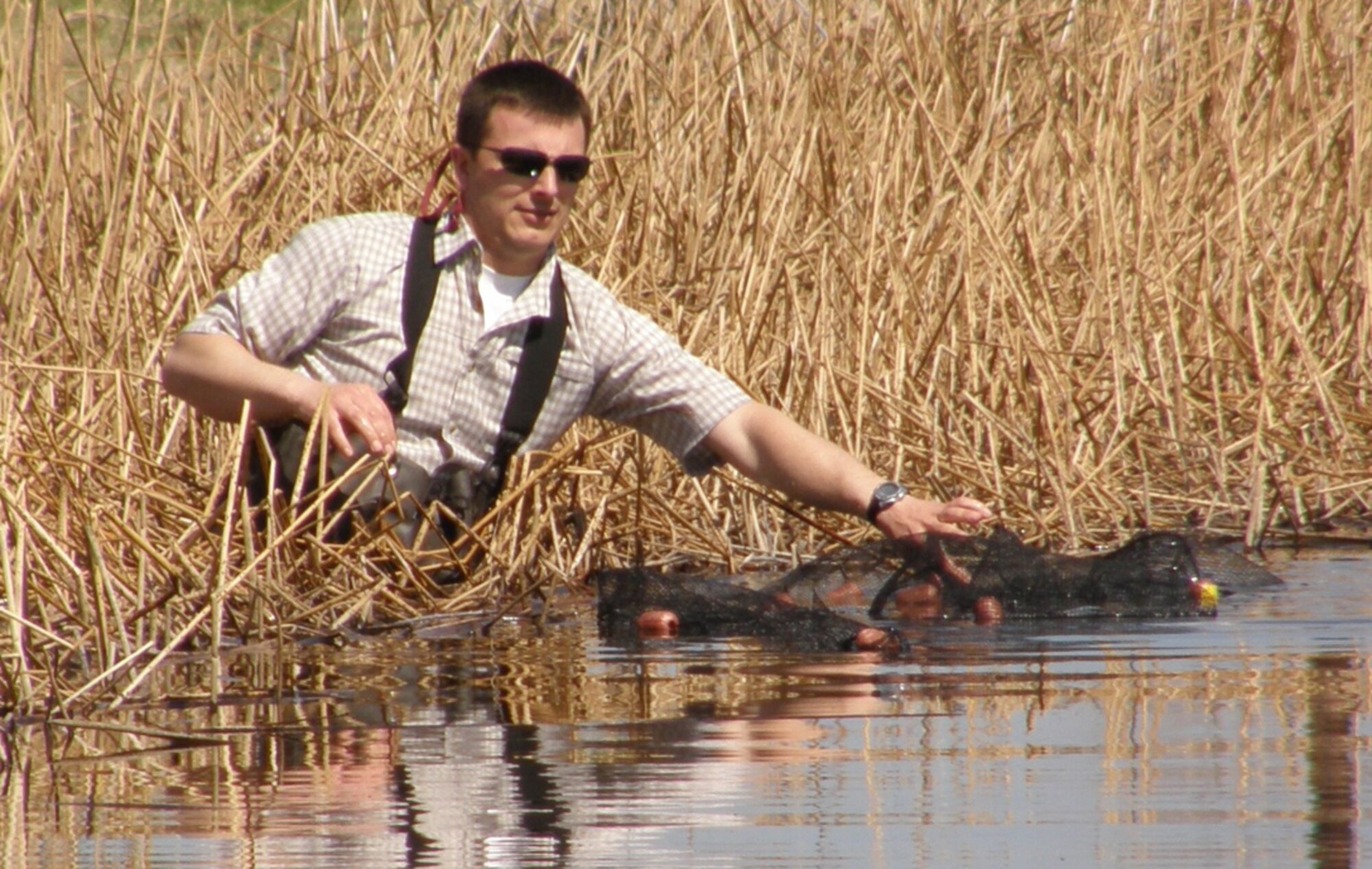 Gibbons gets into the reeds at Powwow Pond to try and net some of the unwanted goldfish that have been introduced into the waters there. Residents are reminded that releasing any fish into the pond is illegal. (U.S. Air Force file photo)