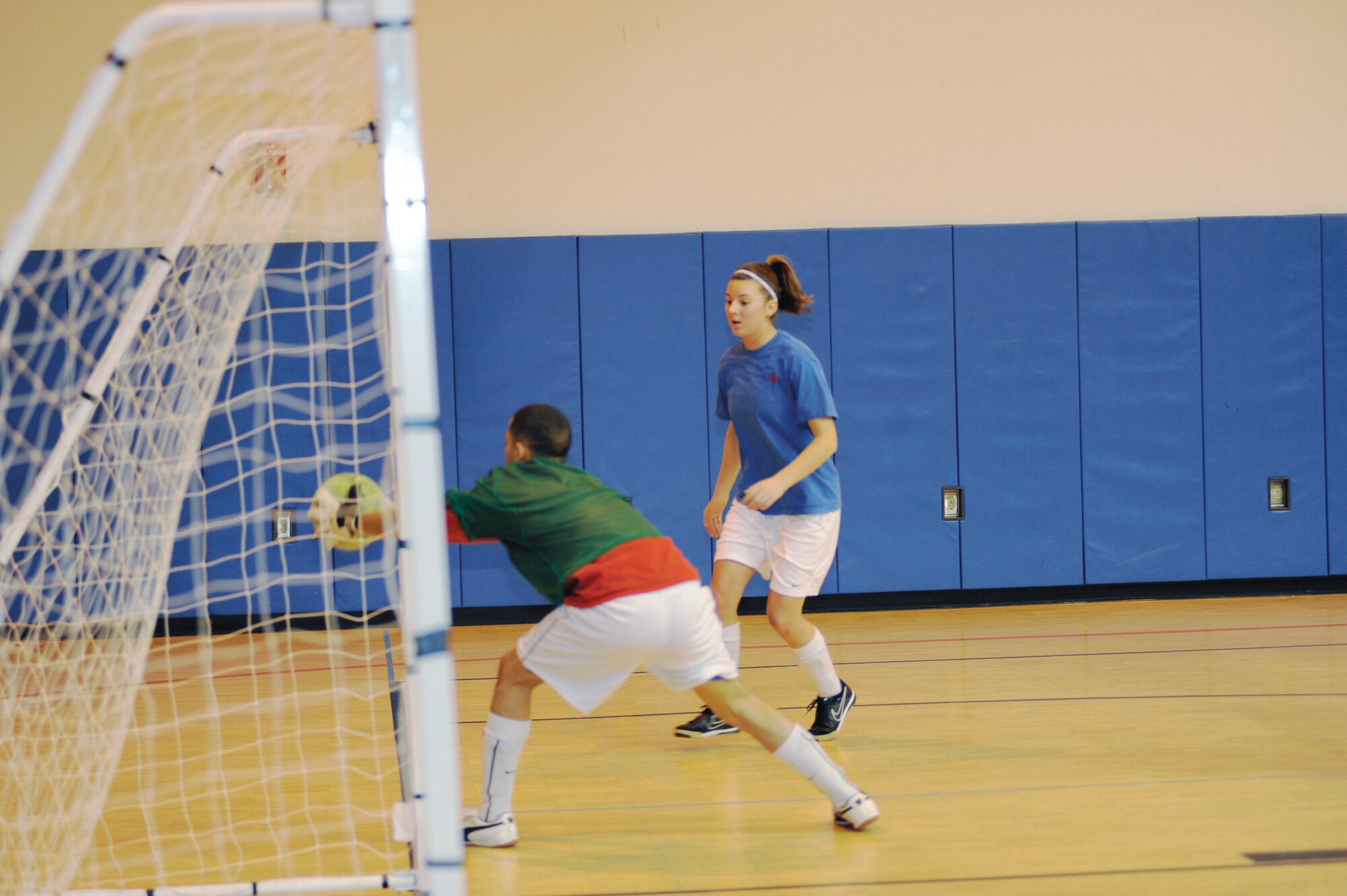 Alfredo Garcia, red, blocks a goal attempt by Danielle Hayes, blue, during the playoff finals between the Army 56th Engineer Company and the Army 381st Intelligence Squadron in the Buckner Physical Fitness Center Nov. 26, 2011. The reds, representing the 56th Engineer Company, beat the blues, representing the 381st Intelligence Squadron, 7 to 4, earning 3rd place in the finals. The Army 95th Chemical Company earned 1st place and the Army F Company 725 earned 2nd place. (U.S. Air Force photo/Staff Sgt. Robert Barnett)