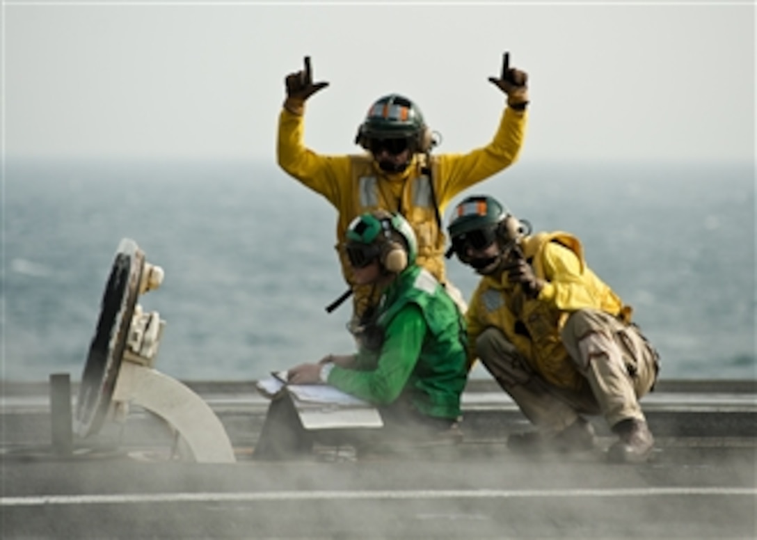 U.S. Navy sailors signal a safety warning as ordnance is armed on an aircraft onboard the aircraft carrier USS John C. Stennis (CVN 74) in the Persian Gulf on Nov. 20, 2011.  The John C. Stennis is deployed to the U.S. 5th Fleet area of responsibility and conducting maritime security operations and support missions as part of Operations Enduring Freedom and New Dawn.  