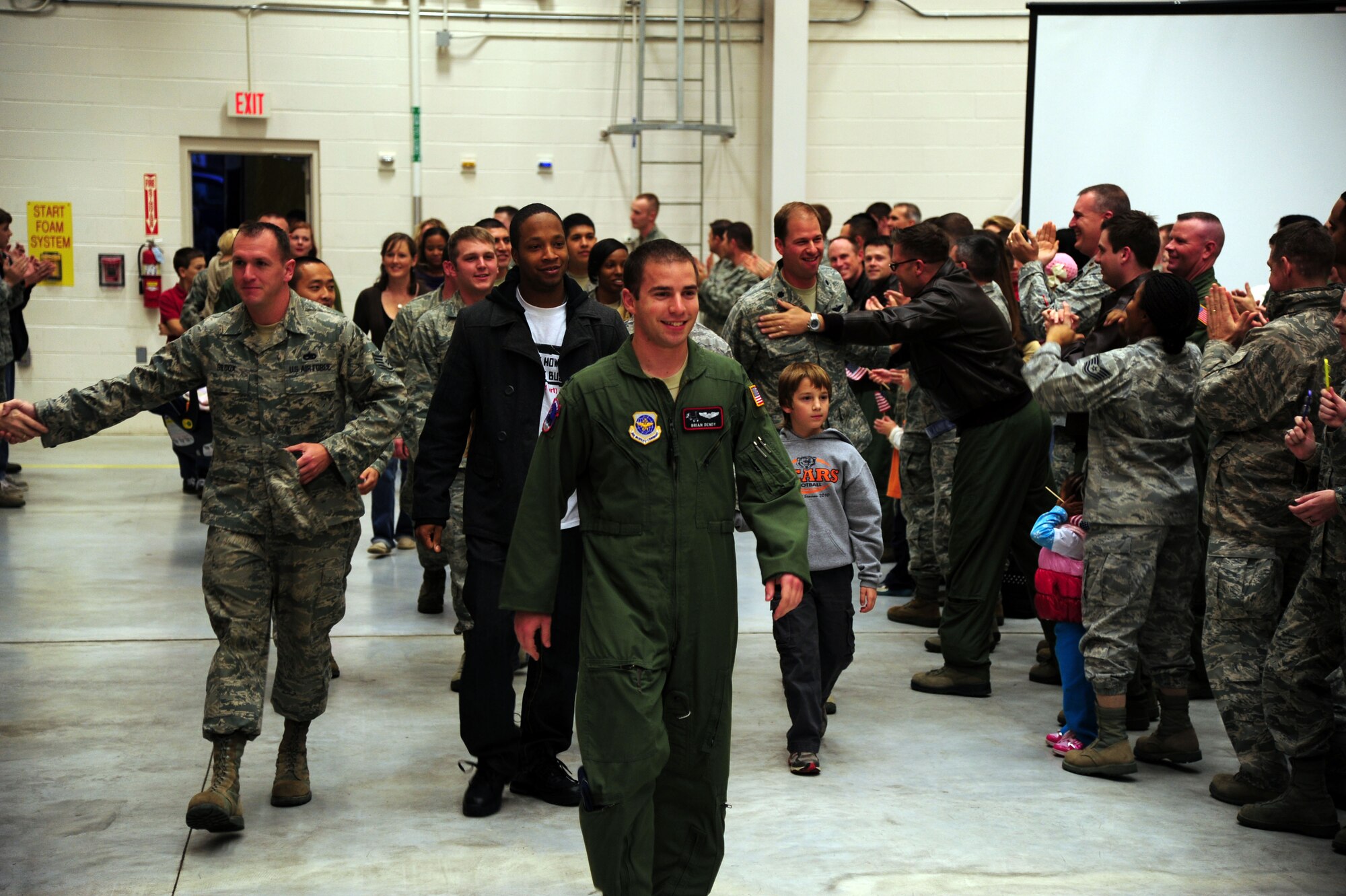 Team Little Rock Airmen, and their families, walk down the aisle to thunderous applause during the Welcome Home Warrior reception for returned deployers Dec. 2, 2011, at Little Rock Air Force Base, Ark. Base Airmen, leaders, civic leaders and actor Judge Reinhold, all gave the returning Combat Airlifters a celebrity reception in an event featuring an inflatable bounce house, petting zoo and dance team. (U.S. Air Force Photo by Airman 1st Class Kaylee Clark)