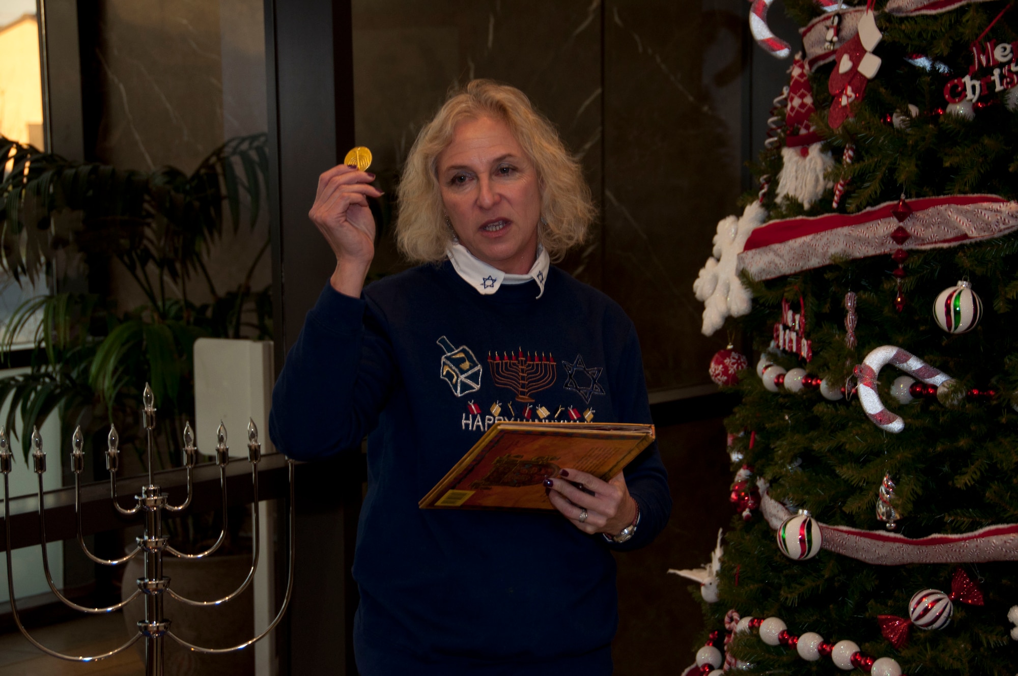 Connie Adelman, a key spouse for Air Force Mortuary Affairs Operations, explains the Jewish tradition of the chocolate coin to the audience at the Charles C. Carson Center for Mortuary Affairs, Dover Air Force Base, Del., Dec. 1, 2011 during a tree lighting ceremony. Giving chocolate coins is a tradition during Hanukkah. (U.S. Air Force photo/Tech. Sgt. Marvin B. Moore)