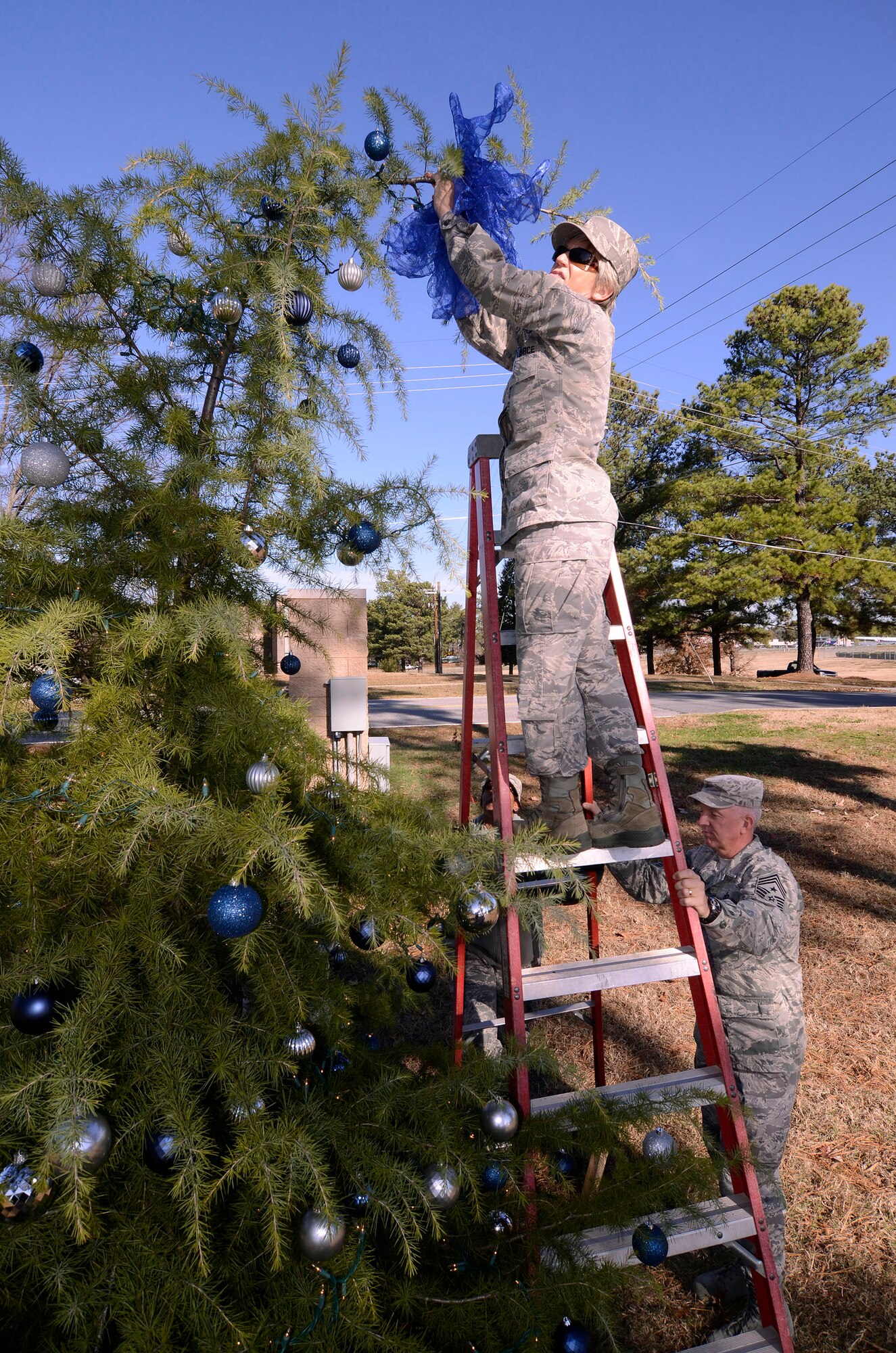 Senior Master Sgt. Joy Hughes, 94th Airlift Wing chief of education, attaches a bow to the top of the wing Christmas tree as Chief Master Sgt. Wendell Peacock, 94th Airlift Wing command chief, steadies the ladder for her, Dec. 2.  (U.S. Air Force photo/ Brad Fallin)