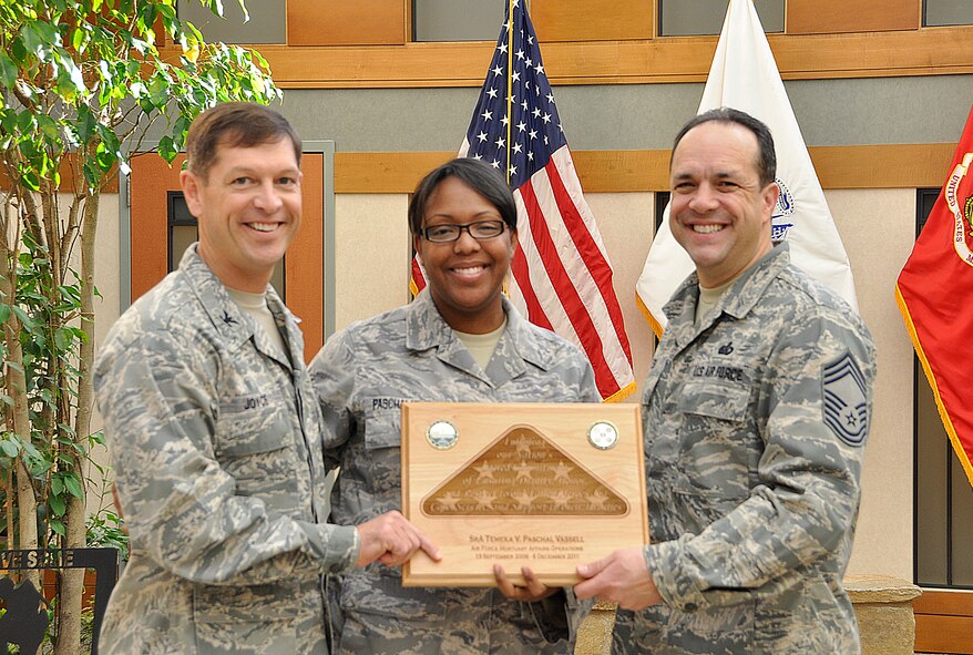 Col. Thomas C. Joyce, Air Force Mortuary Affairs Operations commander, and Chief Master Sgt. David Fish, AFMAO chief enlisted manager, present a going-away plaque to Senior Airman Tameka Paschal-Vassell, Dec. 2, 2011 at the Charles C. Carson Center for Mortuary Affairs. Paschal-Vassell has supported the mortuary mission for more than three years, most recently in the port mortuary administrative section. (U.S. Air Force photo/Christin Michaud)