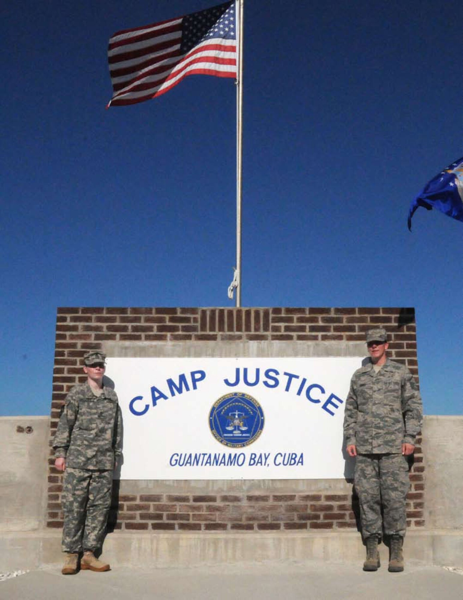 Sisters Army Staff Sgt. Rebecca Abbott and Air Force Master Sgt. Kelly Abbott pose in front of the sign at Camp Justice, Guantanamo Bay, Cuba. Rebecca flew down as a promise to her sister Kelly to help pin on her stripes during her promation to an E-7 during Kelly's deployment to GITMO.