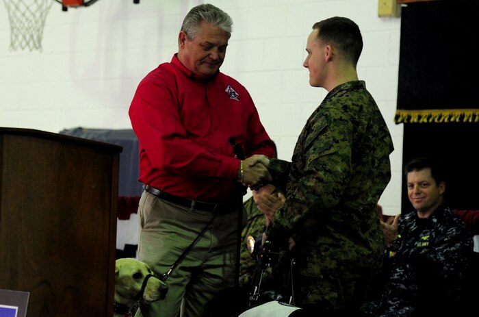 Rick Hairston officially presents Marine Cpl. David Donchess his service dog, Ruth, during a ceremony at the Naval Consolidated Brig Charleston Dec. 1.  The NAVCON Brig, in partnership with Carolina Canines for Service, placed the prisoner-trained, three and a half year-old black lab mix with Donchess, who is a wounded service member. Donchess deployed twice to Helmand Province, Afghanistan with the 1st Battalion, 6th Marine Regiment.  In March 2010, the seven-ton truck he was driving detonated an Improvised Explosive Device. He sustained numerous injuries and was awarded the Purple Heart. CCFS is a non-profit health and human services organization that trains service dogs for people with disabilities. Through this program, military prisoners are taught to train service dogs for veterans with disabilities. Since the program's inception, 14 wounded service members have received service dogs. Hairston is the President of CCFS.  (U.S. Air Force photo/ Staff Sgt. Nicole Mickle)  
