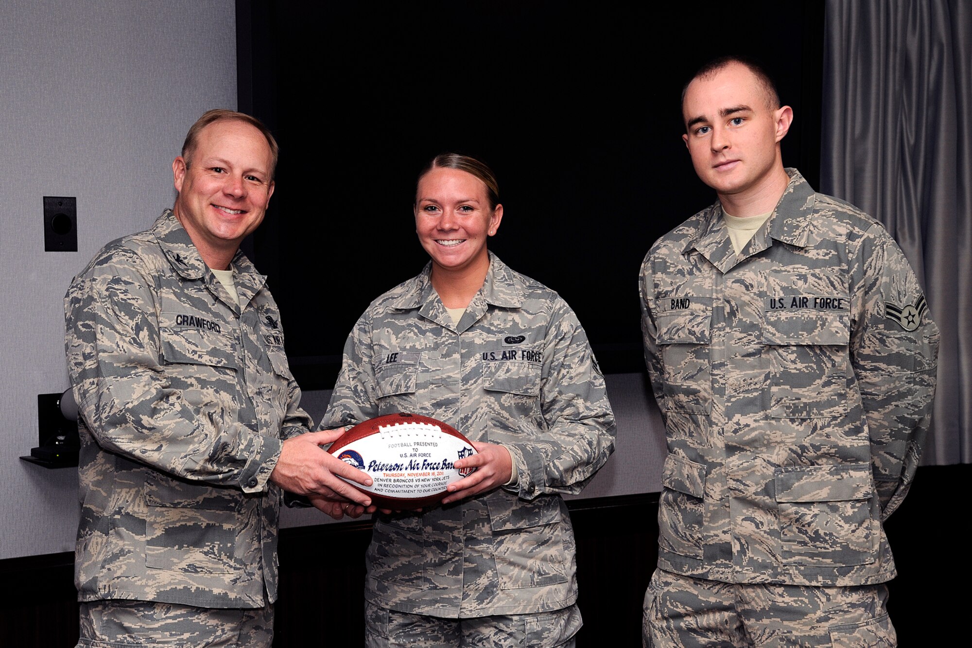 PETERSON AIR FORCE BASE, Colo. – Col. Chris Crawford (left) accepts a ceremonial Denver Broncos football from Airmen 1st Class Katie Lee (center) and Ryan Band, Nov. 30 in the wing conference room. Lee, Band and 23 Airmen from the 21st Space Wing attended the Broncos military salute game Nov. 17 in Denver, where the Airmen were recognized during a pre-game ceremony. The Airmen then watched the game, as the Broncos beat the New York Jets 17-13. (U.S. Air Force photo/Craig Denton)