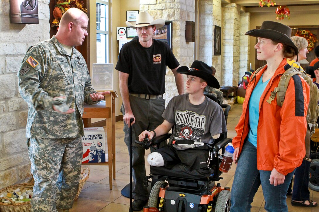 Army Maj. Stephen Short, with Army North's public affairs office, talks to Army Pfc. Kevin Trimble, his brother, Ben, also a soldier, and his sister, Deborah, an airman, as they arrive at the at the Warrior and Family Support Center in San Antonio, Nov. 10, 2011. Pfc. Trimble lost both legs and an arm in a roadside bomb blast in Afghanistan and is recovering on Fort Sam Houston. He takes a leather tooling class at the center.