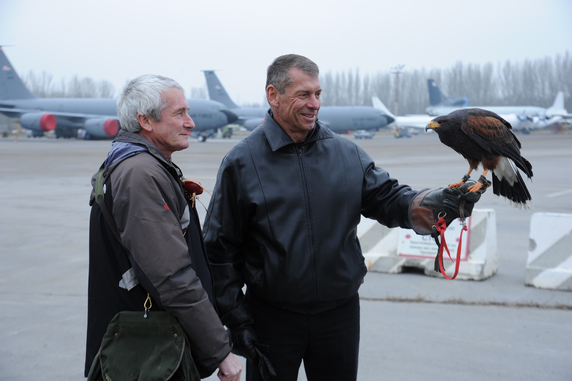 Vince McMahon, World Wrestling Entertainment CEO, holds on to Jet, a hawk, as Steve Farrell, 376th Air Expeditionary Wing flight safety, watches during the Armed Forces Entertainment Handshake Tour visit to the Transit Center at Manas, Kyrgyzstan, Dec. 2. McMahon visited with troops on his first AFE tour to Manas with WWE entertainers Kofi Kingston, and Nikki and Brie Bella. Hawks are used to deter other birds from nesting on the airfield and causing aircraft bird strikes. (U.S. Air Force photo/Tech. Sgt. Hank Hoegen)