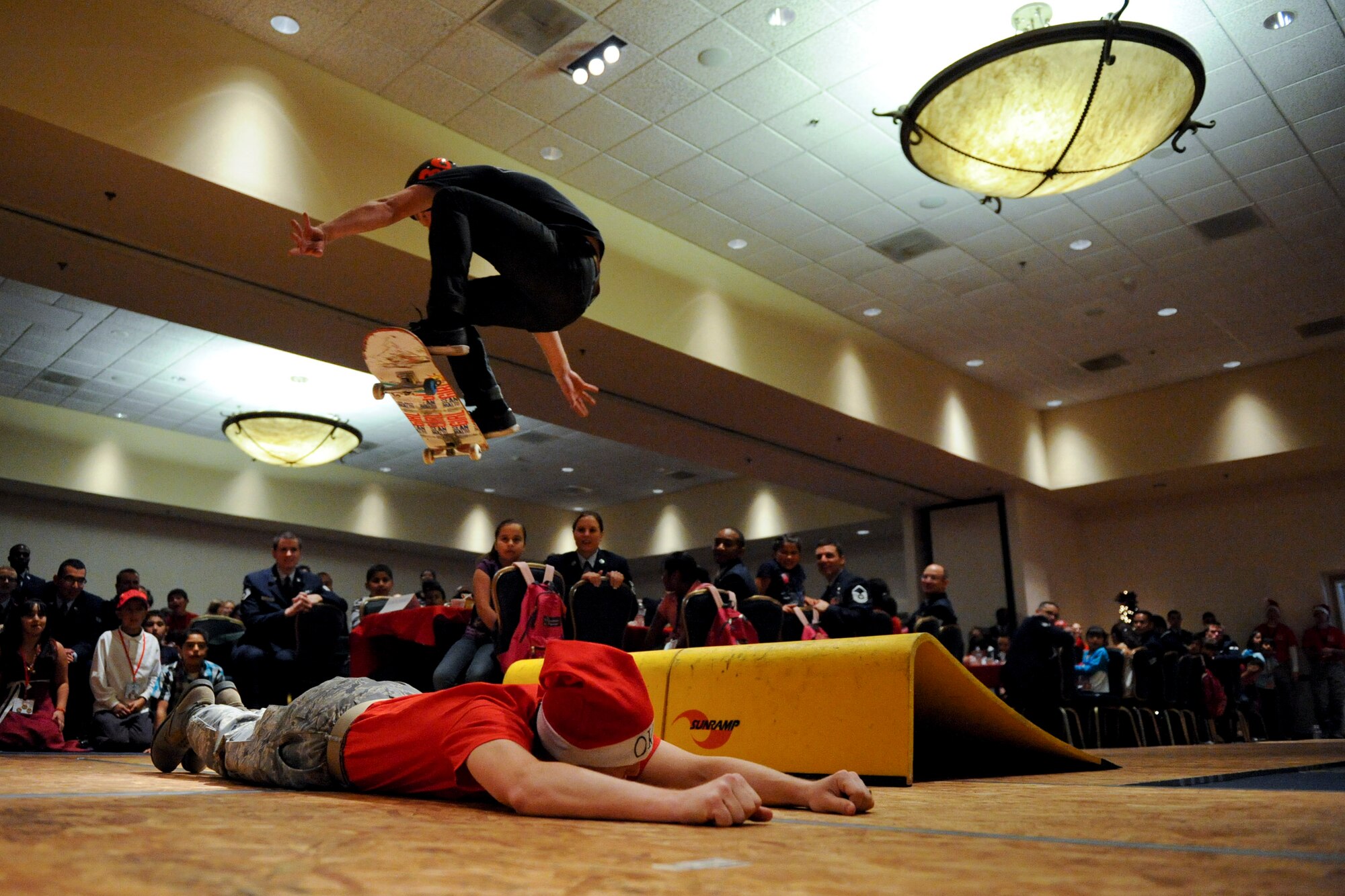 VANDENBERG AIR FORCE BASE, Calif. --A skater from a local demonstration team jumps over a volunteer during Operation Kids Christmas at the Pacific Coast Club here Saturday, Dec. 3, 2011. OKC is an annual event, organized and run by a private organization, in which approximately 200 local children are brought on base and given the opportunity to play games, meet Santa and enjoy the companionship of volunteer military members. (U.S. Air Force/Staff Sgt. Levi Riendeau)