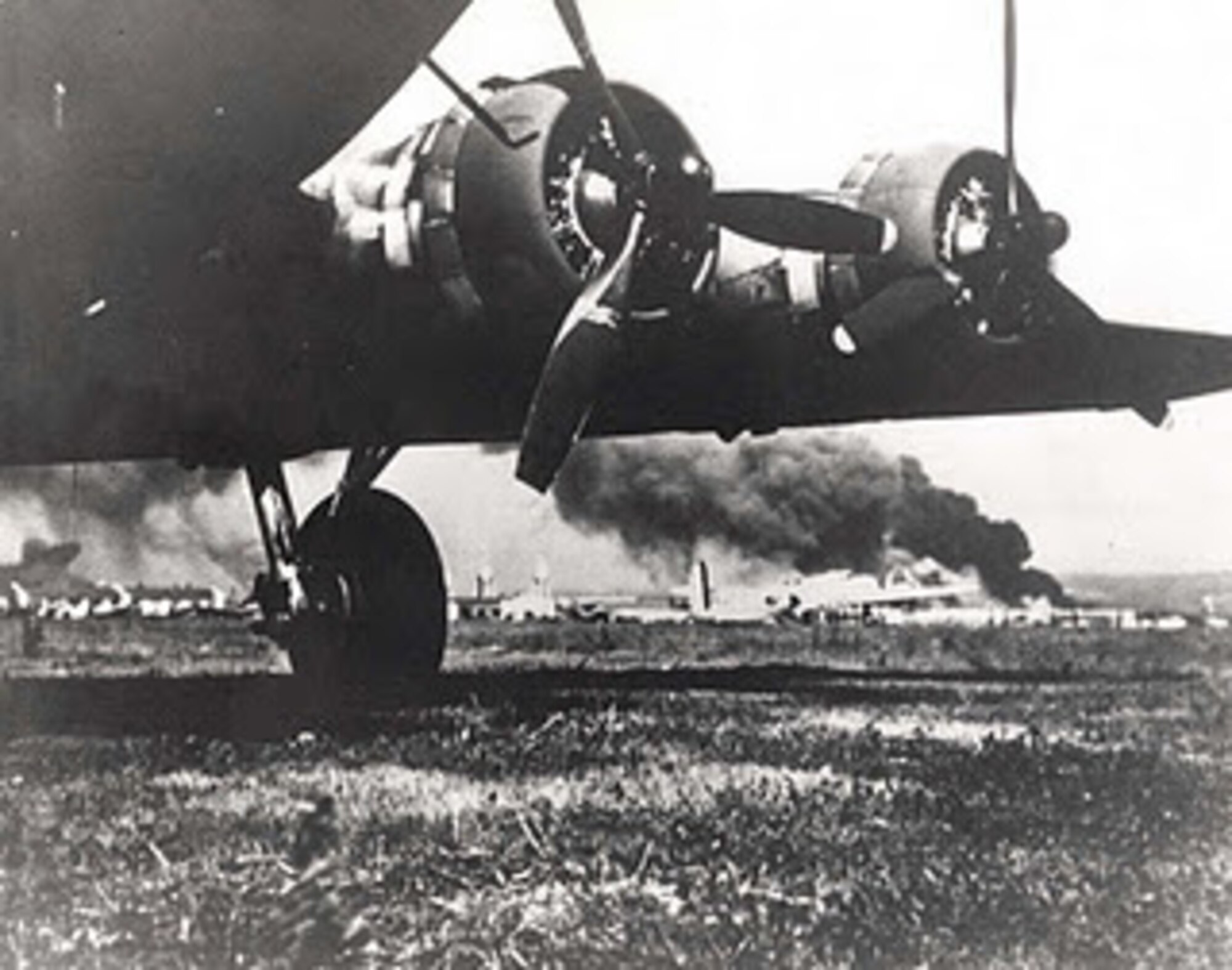 B-17 frames the devastating results from Japanese attack on Hickam Field, December 7, 1941. The smoke in the background is from USS Arizona which Japanese bombed. The B-17s arrived at Hickam the morning of the attack. (Courtesy photo)