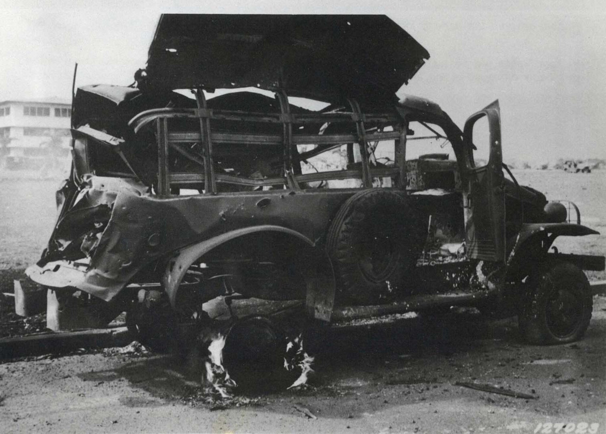 Heavily damaged truck at Hickam Field next to parade grounds with big barracks in background, Dec 7, 1941.