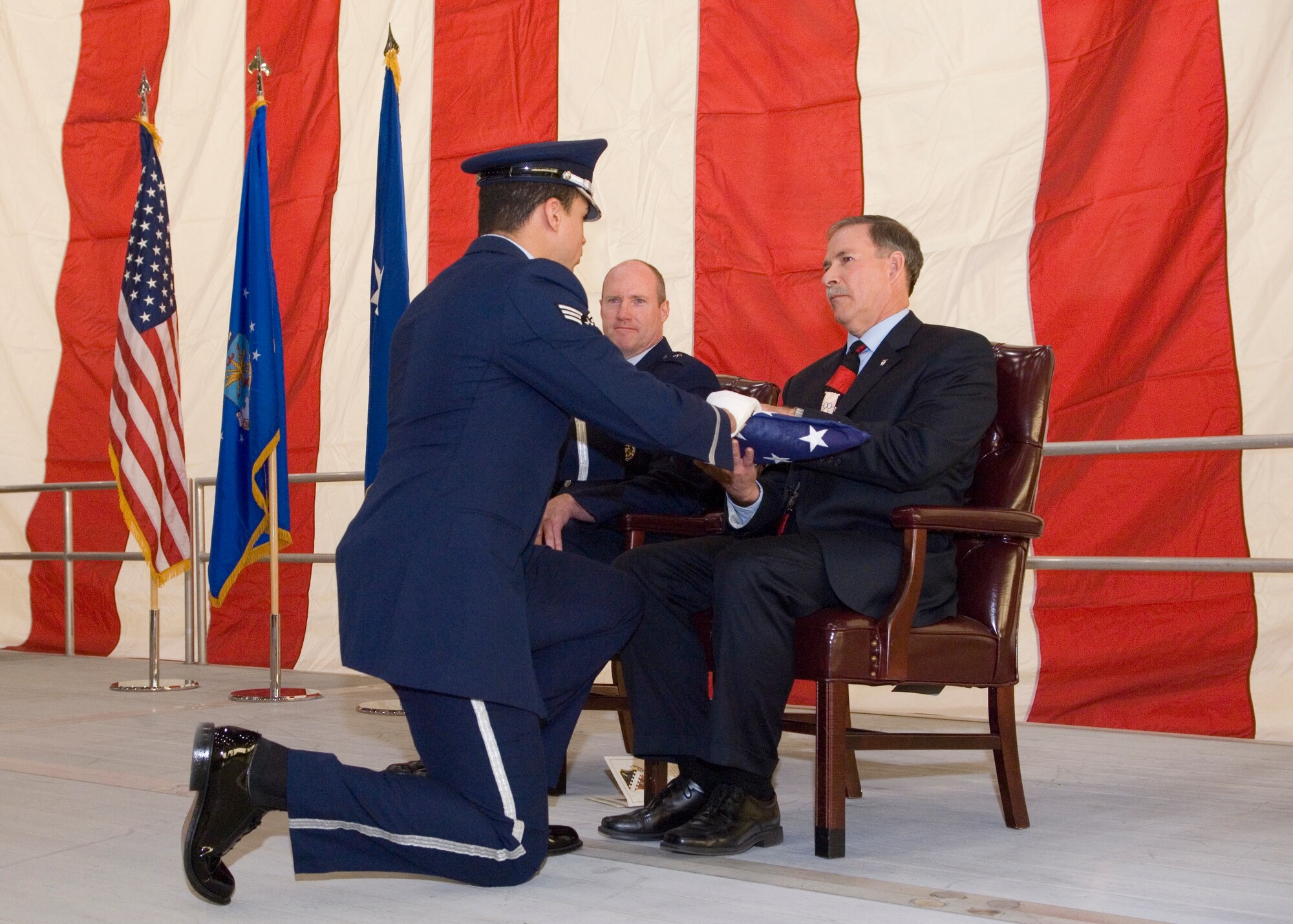 With Brig. Gen. Robert C. Nolan II, Air Force Flight Test Center commander looking on, Thomas Berard is presented a folded American flag from a member of the Blue Eagle Honor Guard during his retirement ceremony, Dec. 2, in Hangar 1600. Out of his 33 year career, Berard gave 28 years of service to Edwards AFB and the AFFTC, serving as project manager and director on many projects, and most recently in senior executive service. (Air Force photo/Edward Cannon)